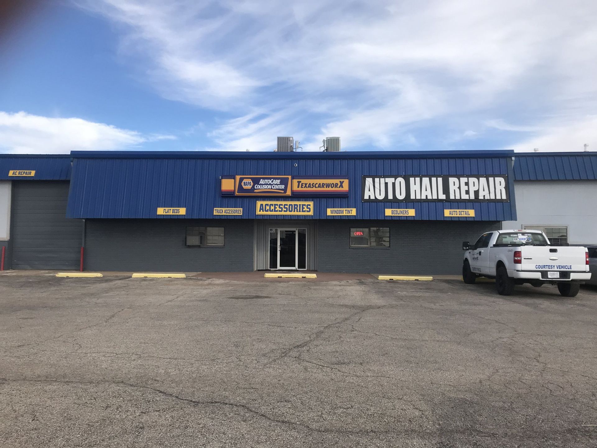 Blue auto repair shop with large “AUTO HAIL REPAIR” sign and a white pickup truck parked outside.
