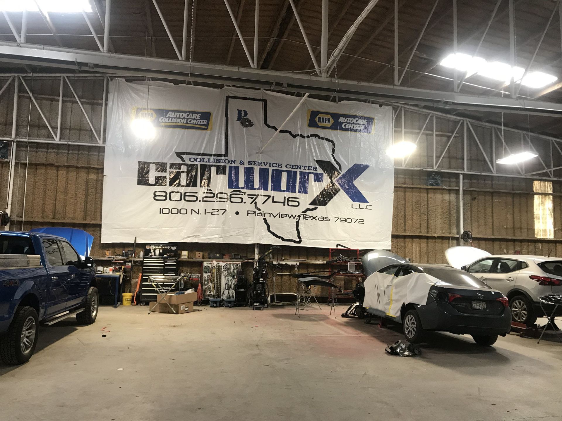 Auto garage interior with a large white banner, parked vehicles, and equipment under bright industrial lights