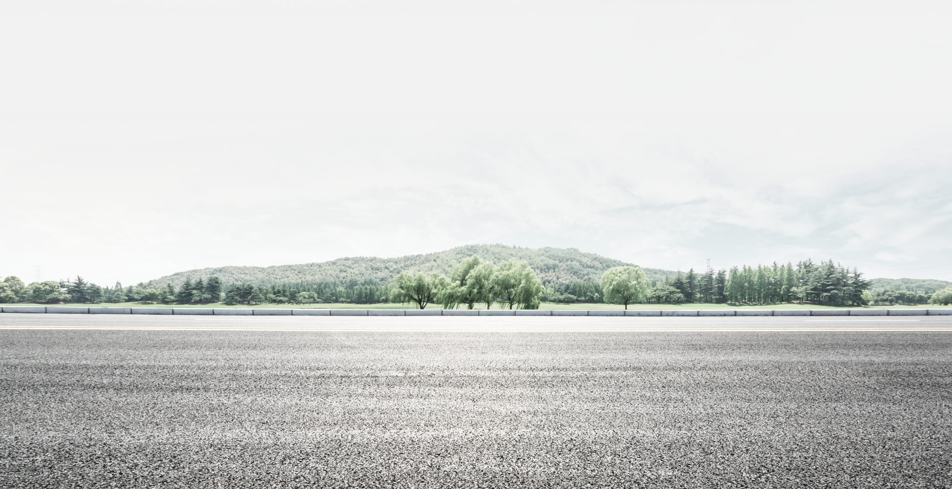 Wide asphalt road with a distant green hill under a pale sky