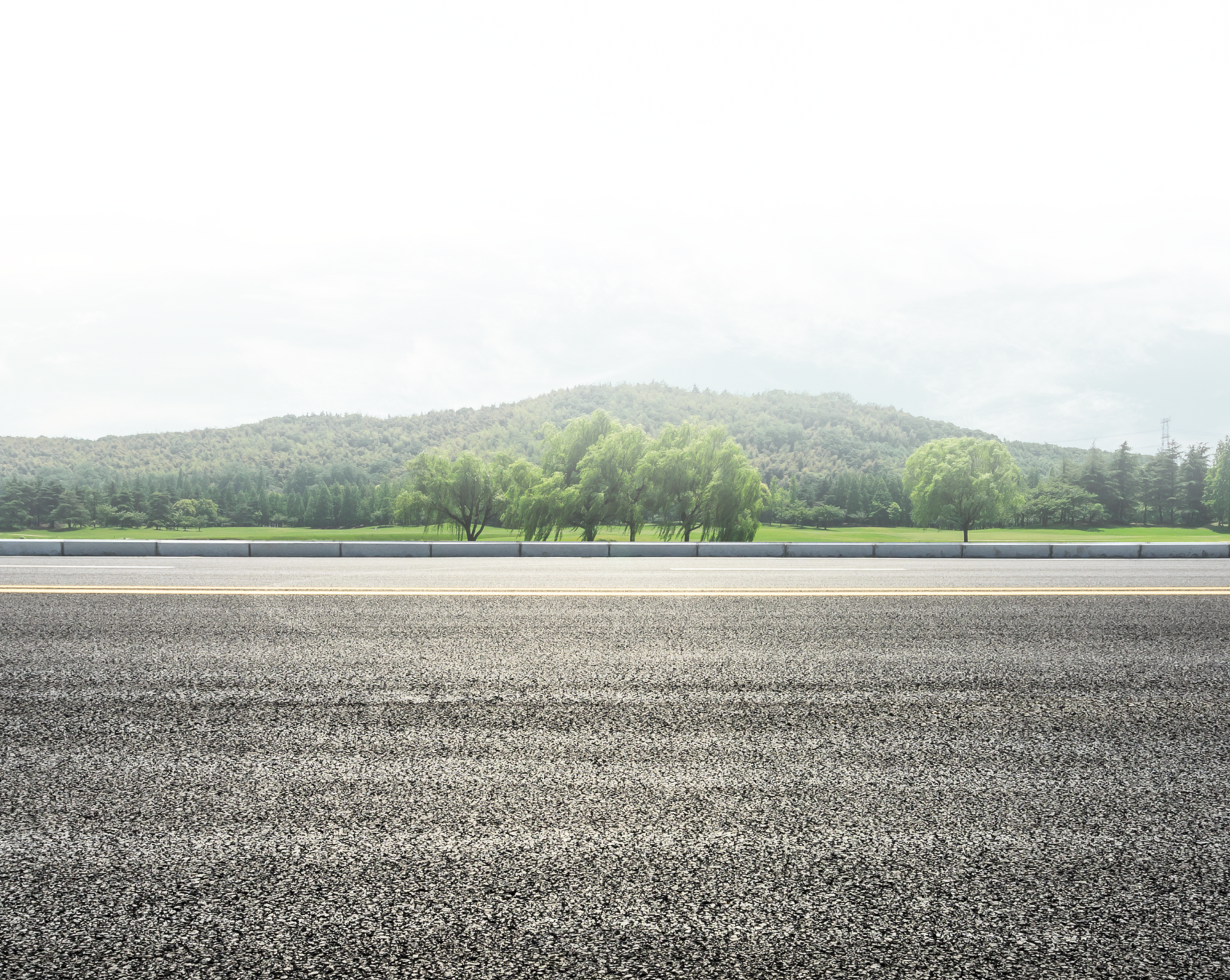 Gravel road in the foreground with a green tree-covered hill in the distance under a bright sky