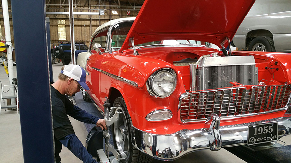 Mechanic working on the front wheel of a red classic car in a garage, hood open | Texas Carworx