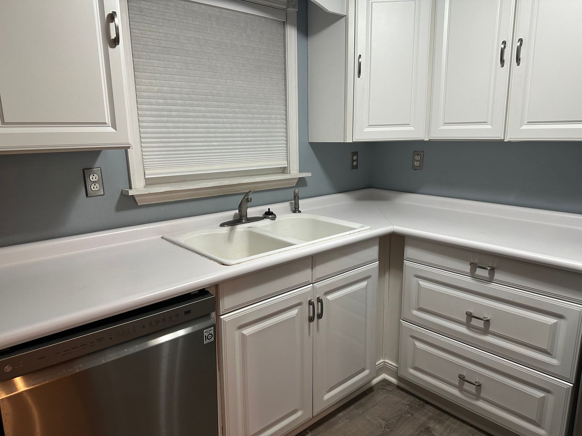 White kitchen cabinets and countertops with a stainless steel dishwasher, and a double sink.