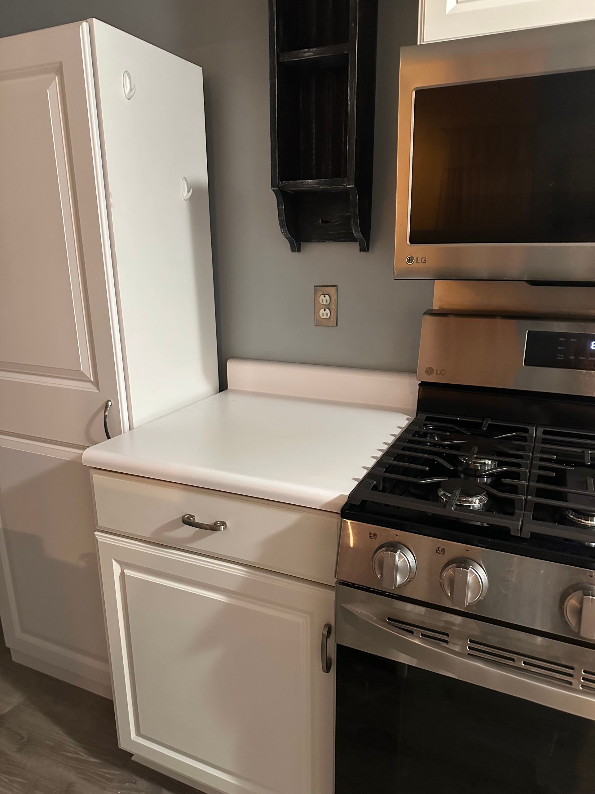 White kitchen cabinets with a stovetop and wall-mounted shelves against a gray wall.