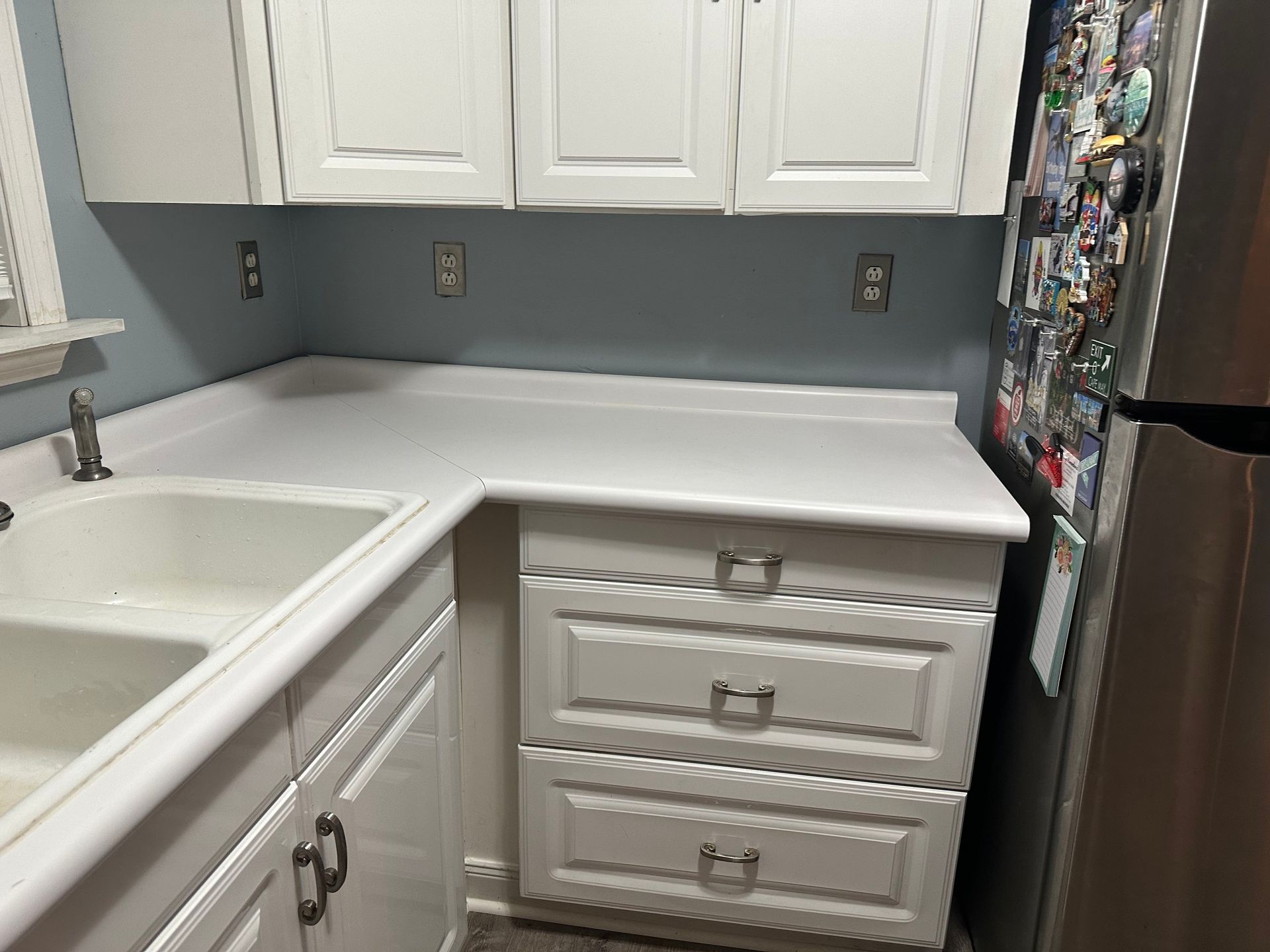 White kitchen cabinets and countertops with a double sink, drawers, and wall outlets.