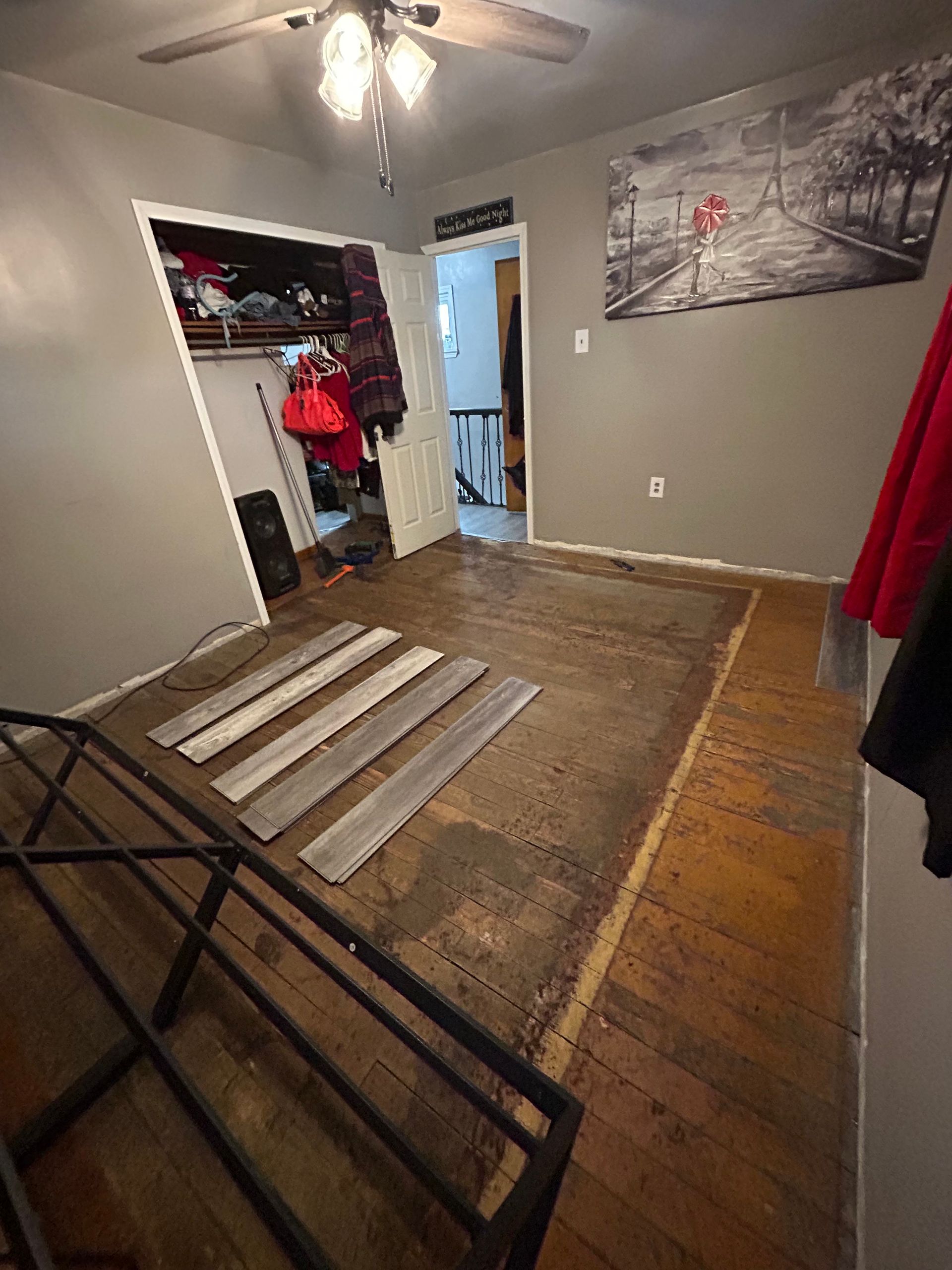 Room with exposed wooden floor and new planks. Closet on the left and doorway on the right. Painting on the wall.