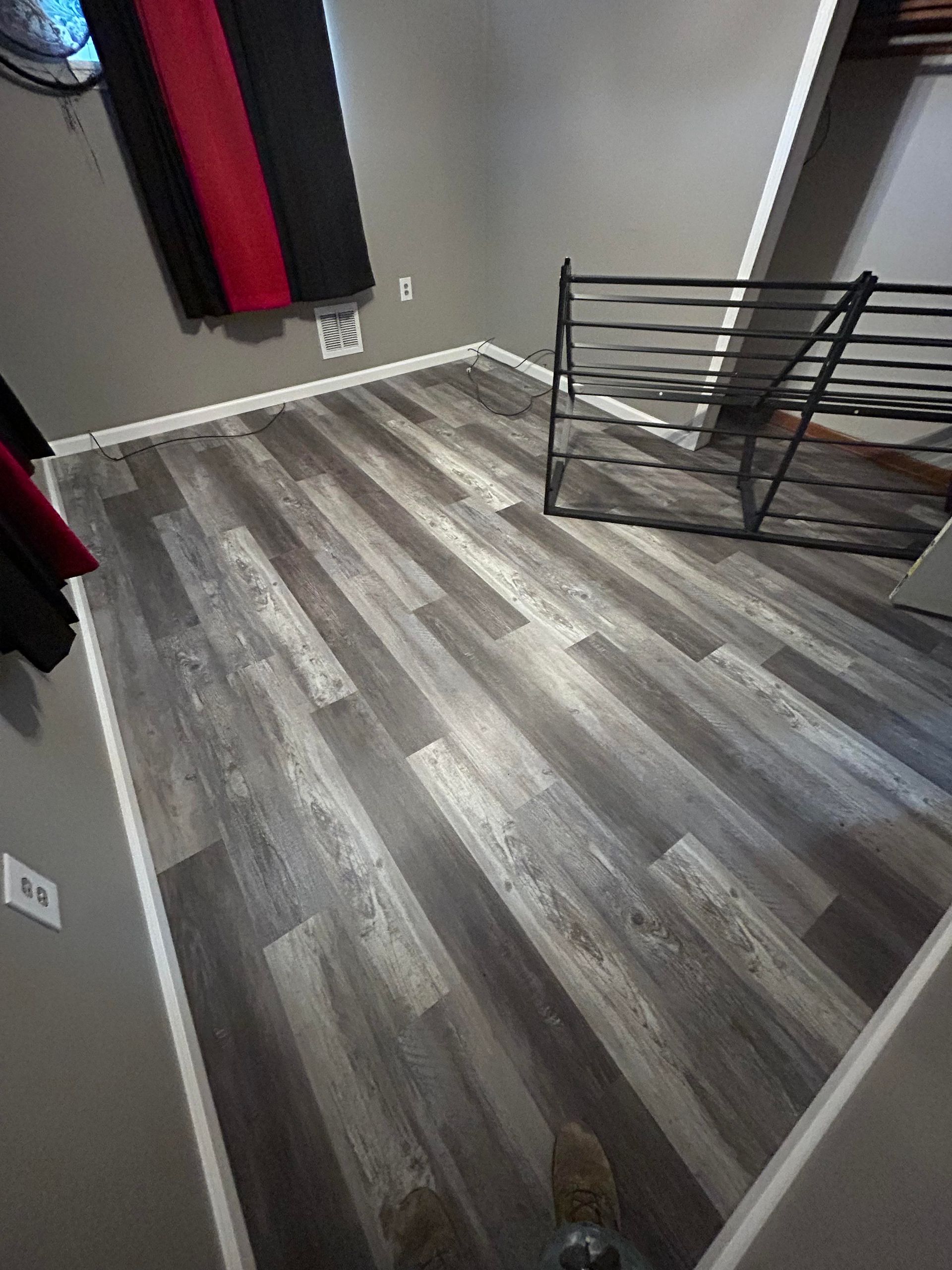 Gray wood-look flooring in a room with a black and red curtain and metal shelving.