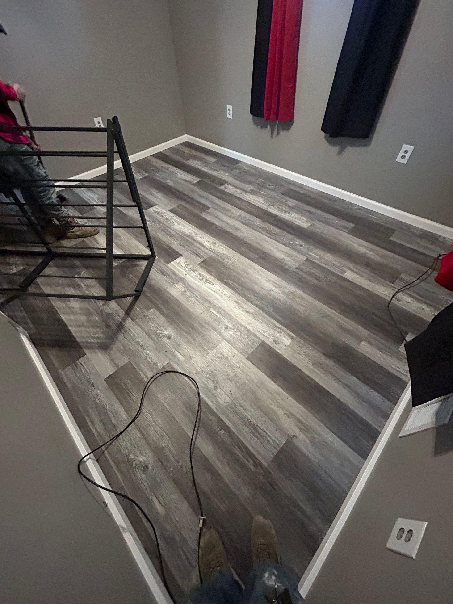 Wooden floor in a gray-walled room with a person, a metal ladder, and black and red curtains.