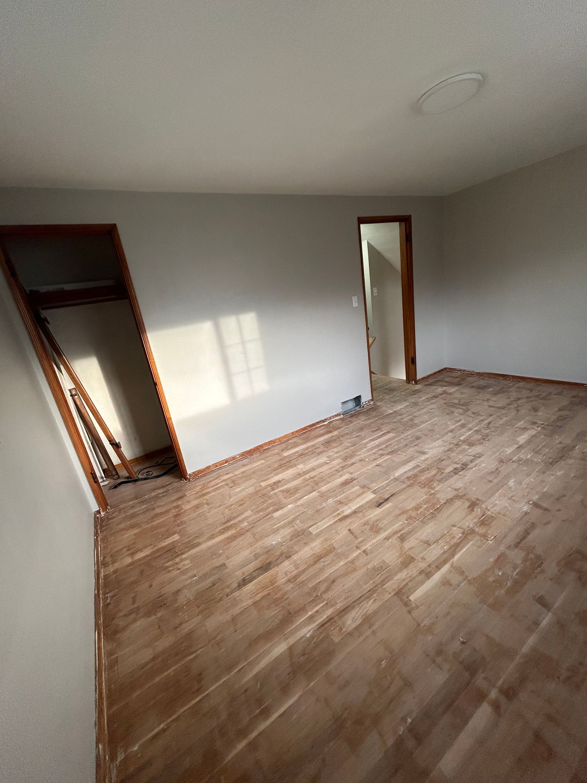 Empty room with wood floors, closet, door, and natural light.