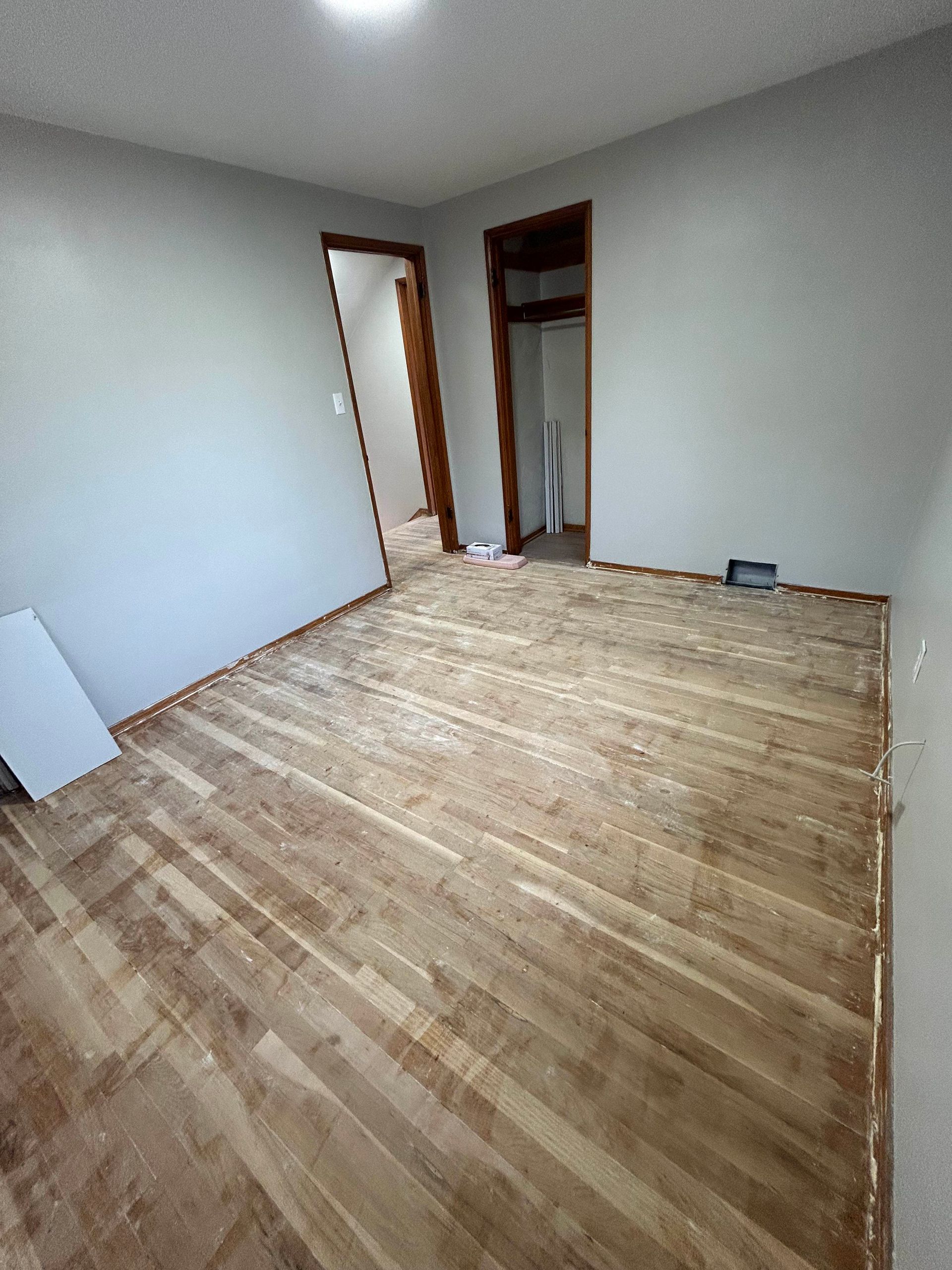 Empty room with unfinished hardwood floor, grey walls, and two open doorways.