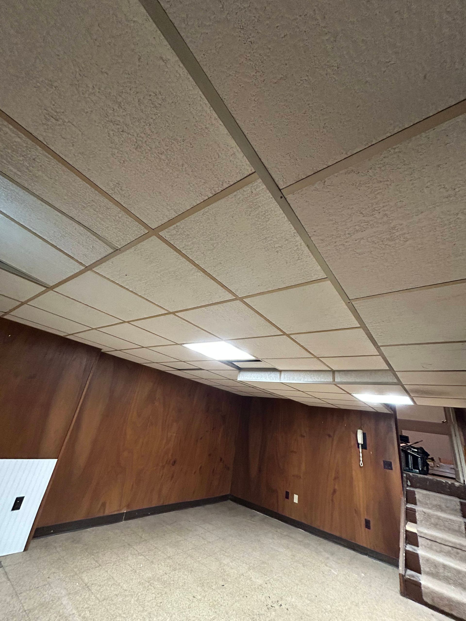 Basement interior with textured ceiling, wood paneling, carpet, and stairs.