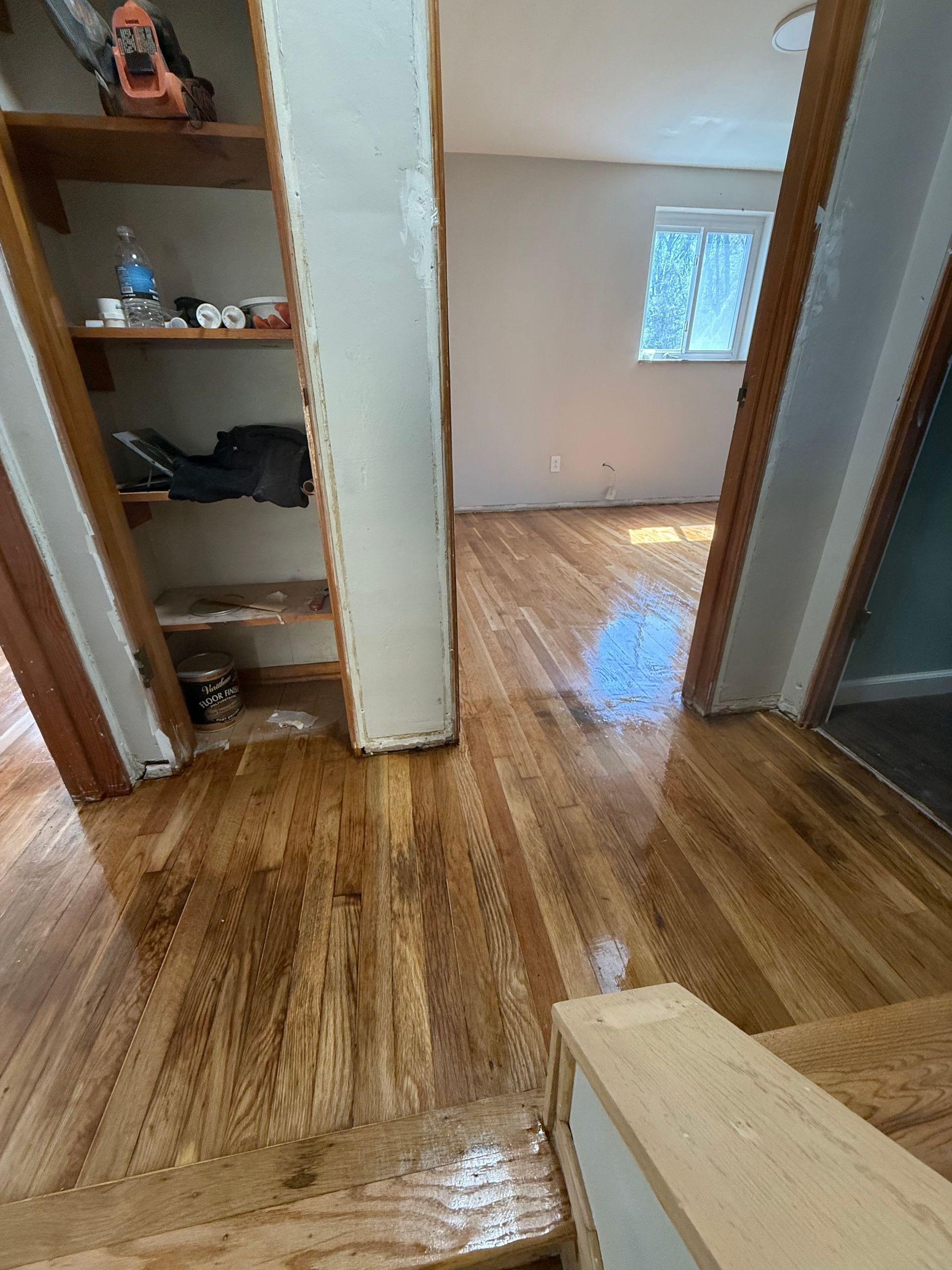 Newly finished hardwood floors in a home. Open doorway to a room with a window, built-in shelving unit.