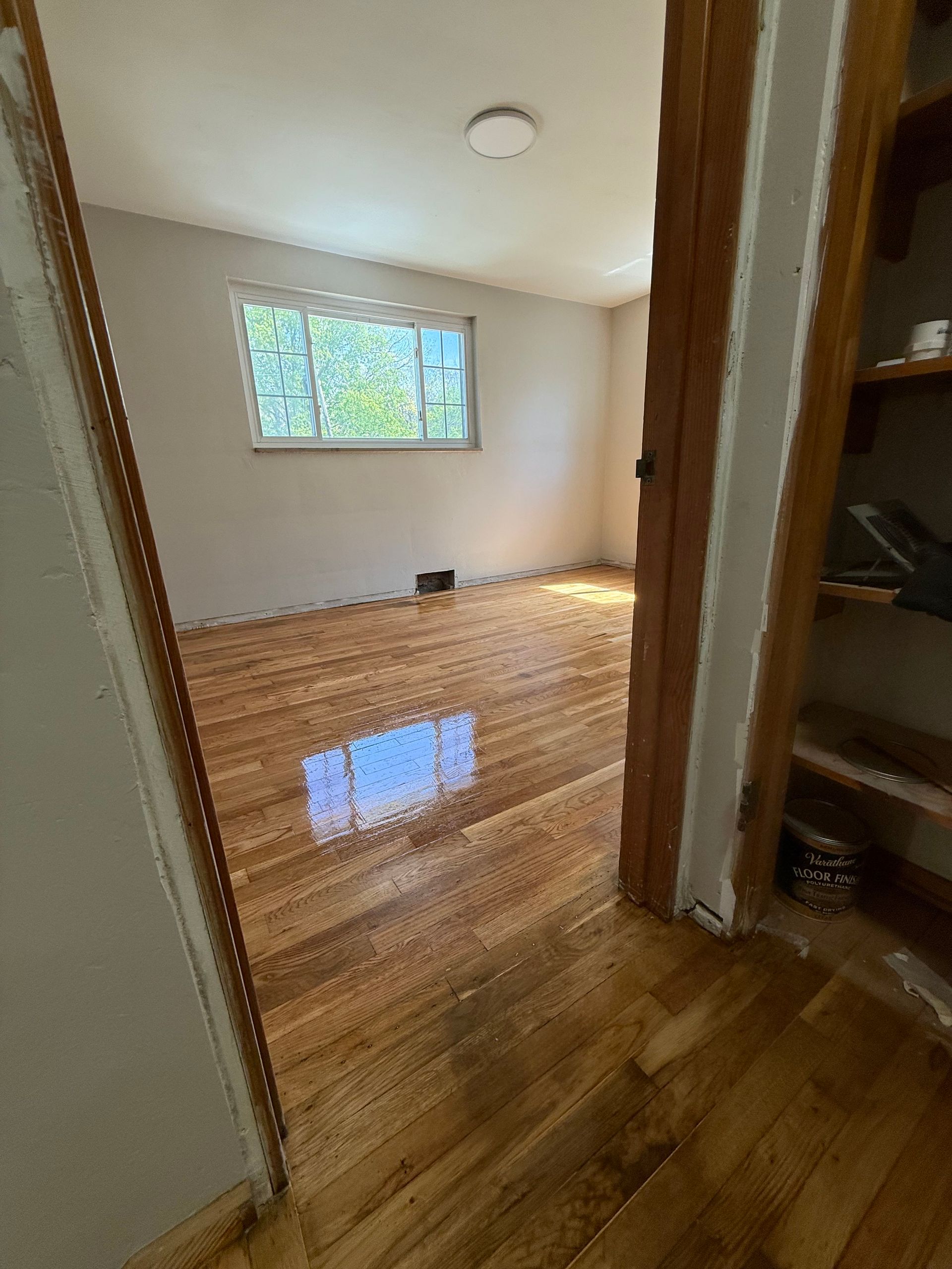 Room with wood floor, window, and open doorway to storage. Light from window reflects on floor.