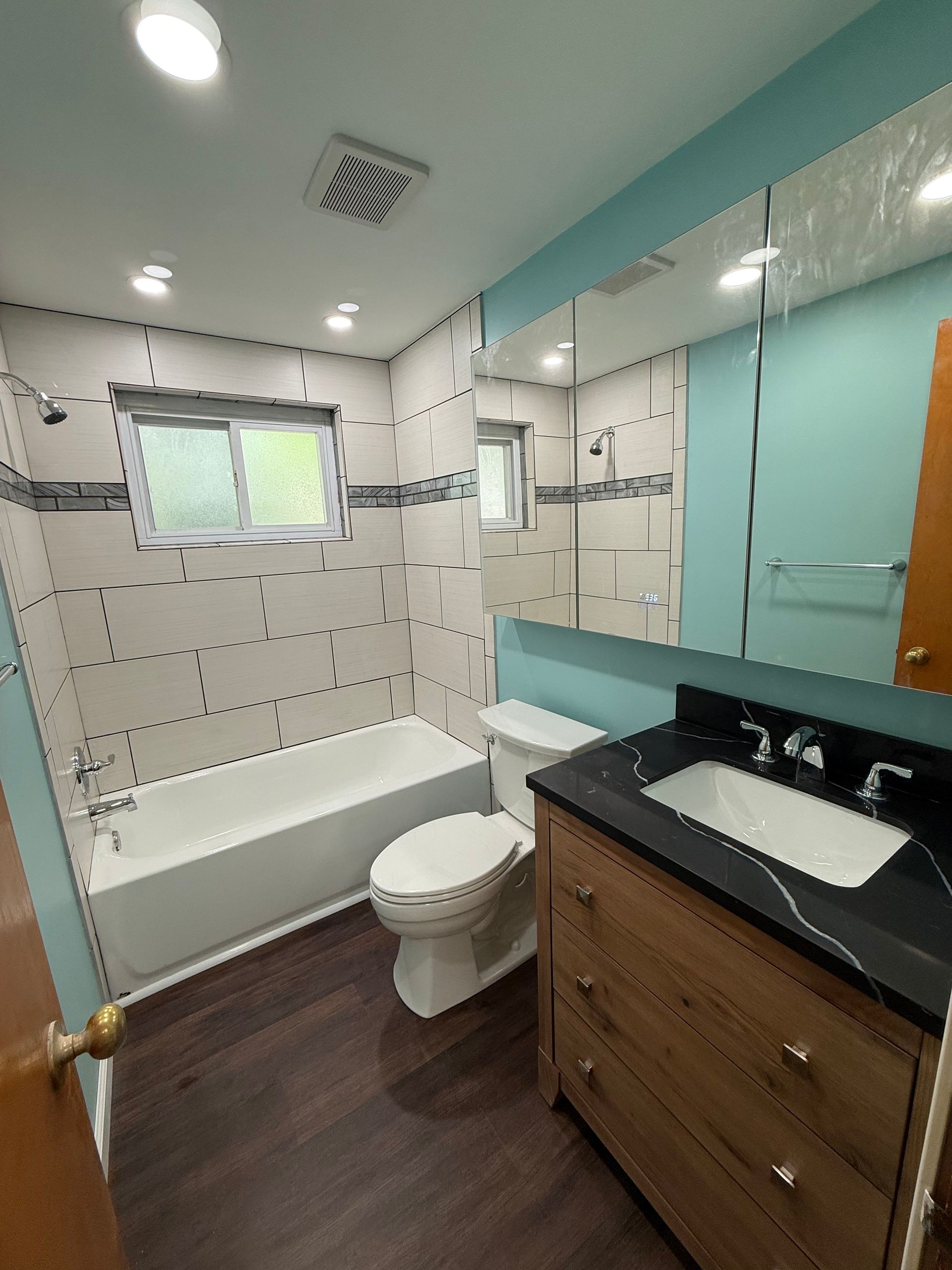 Bathroom with white and black tiled walls, a wooden vanity, and a bathtub.