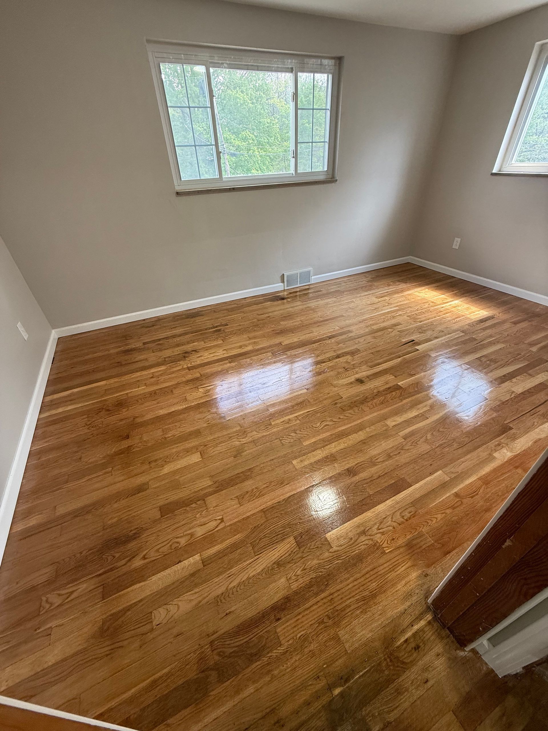Empty room with hardwood floors, two windows, and neutral-colored walls.