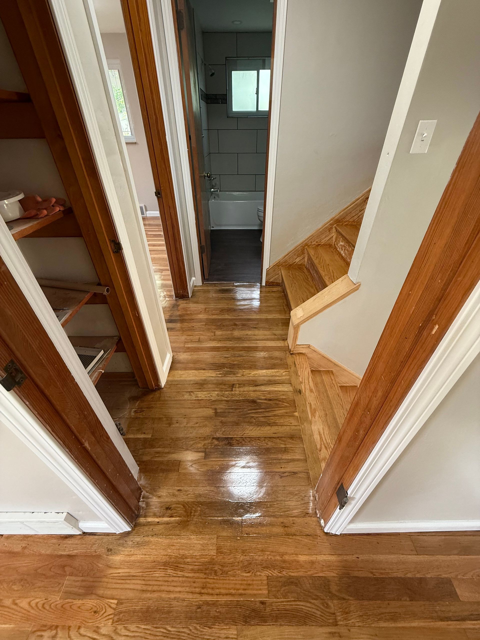Wooden hallway with stairs, doorway to storage, leading to a garage door.