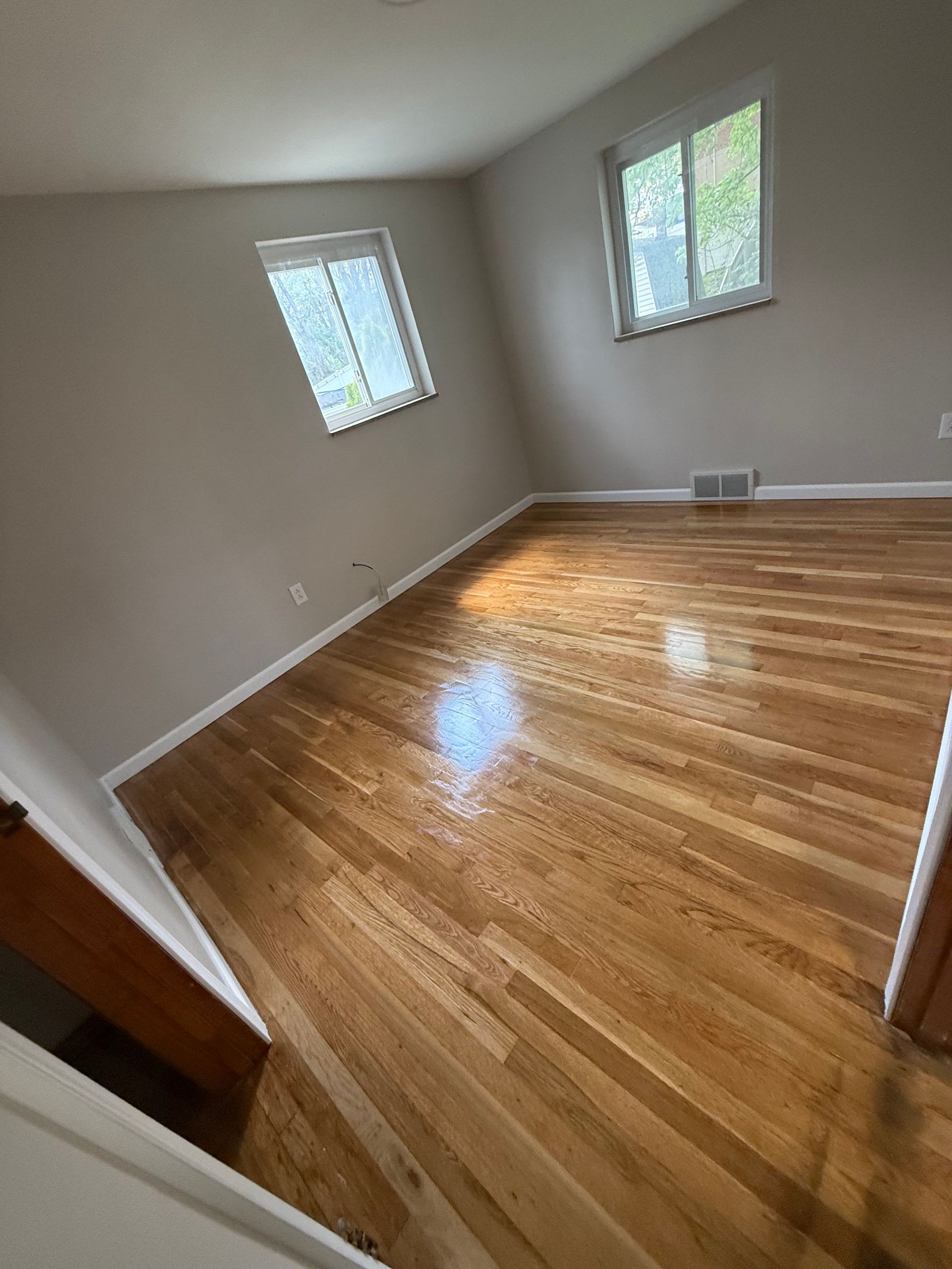 Empty room with hardwood floors, two windows, and neutral walls.