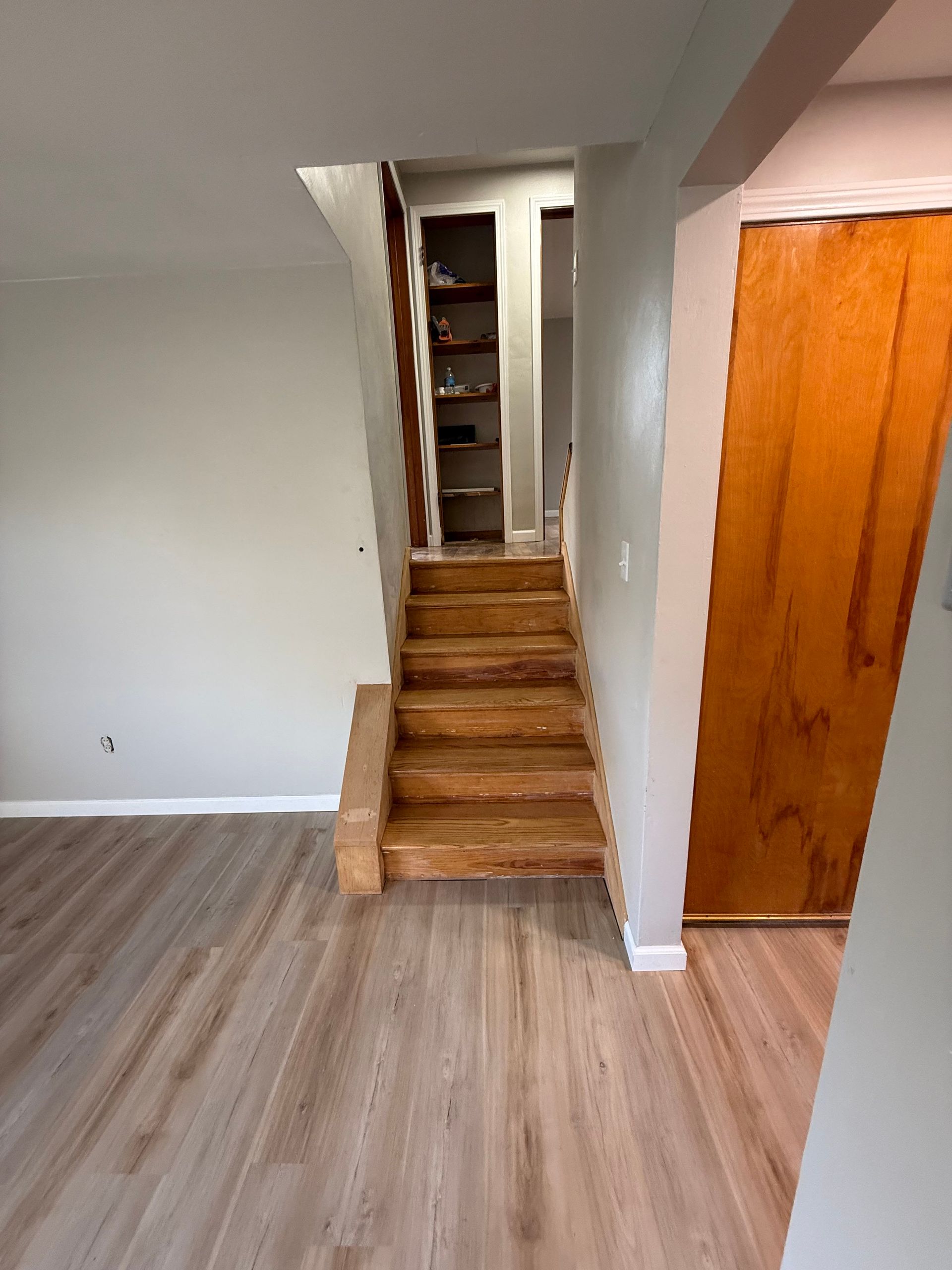 Wooden staircase leading upwards, set between gray walls and a wooden door. Light gray flooring.