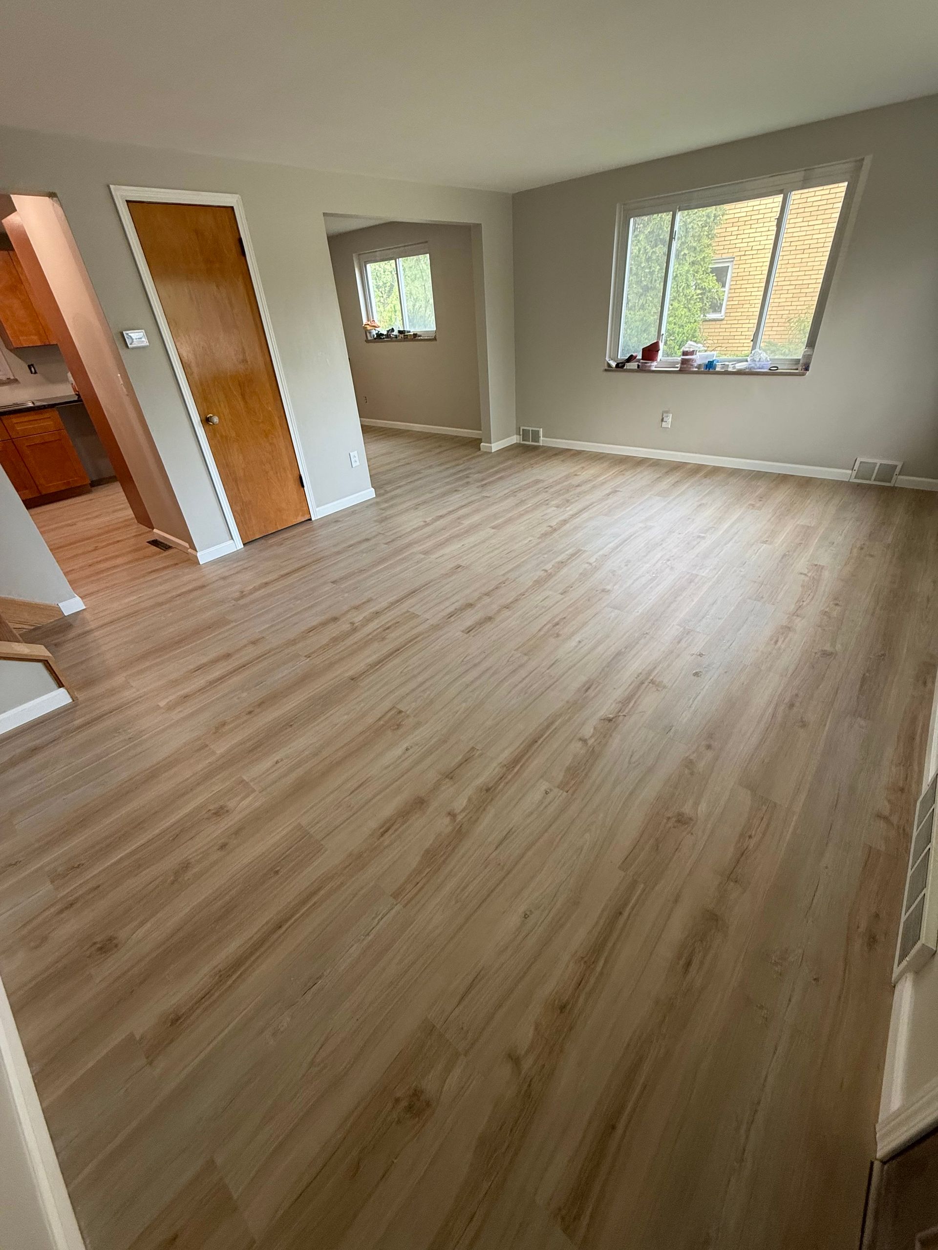 Empty room with light wood-look flooring, gray walls, and a closed wooden door. A window provides natural light.