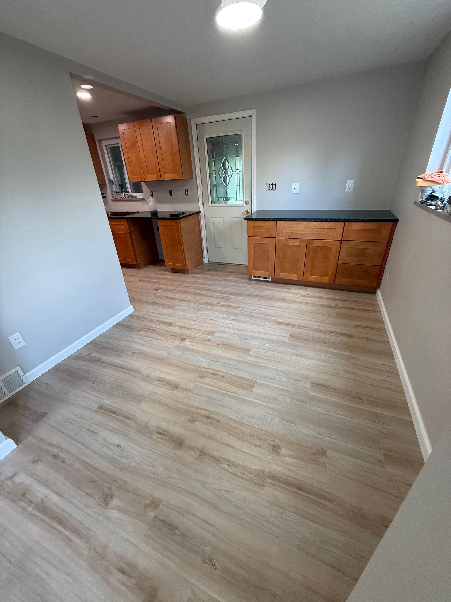 Kitchen with light wood-look flooring, light gray walls, and wood cabinets. A door leads outside.