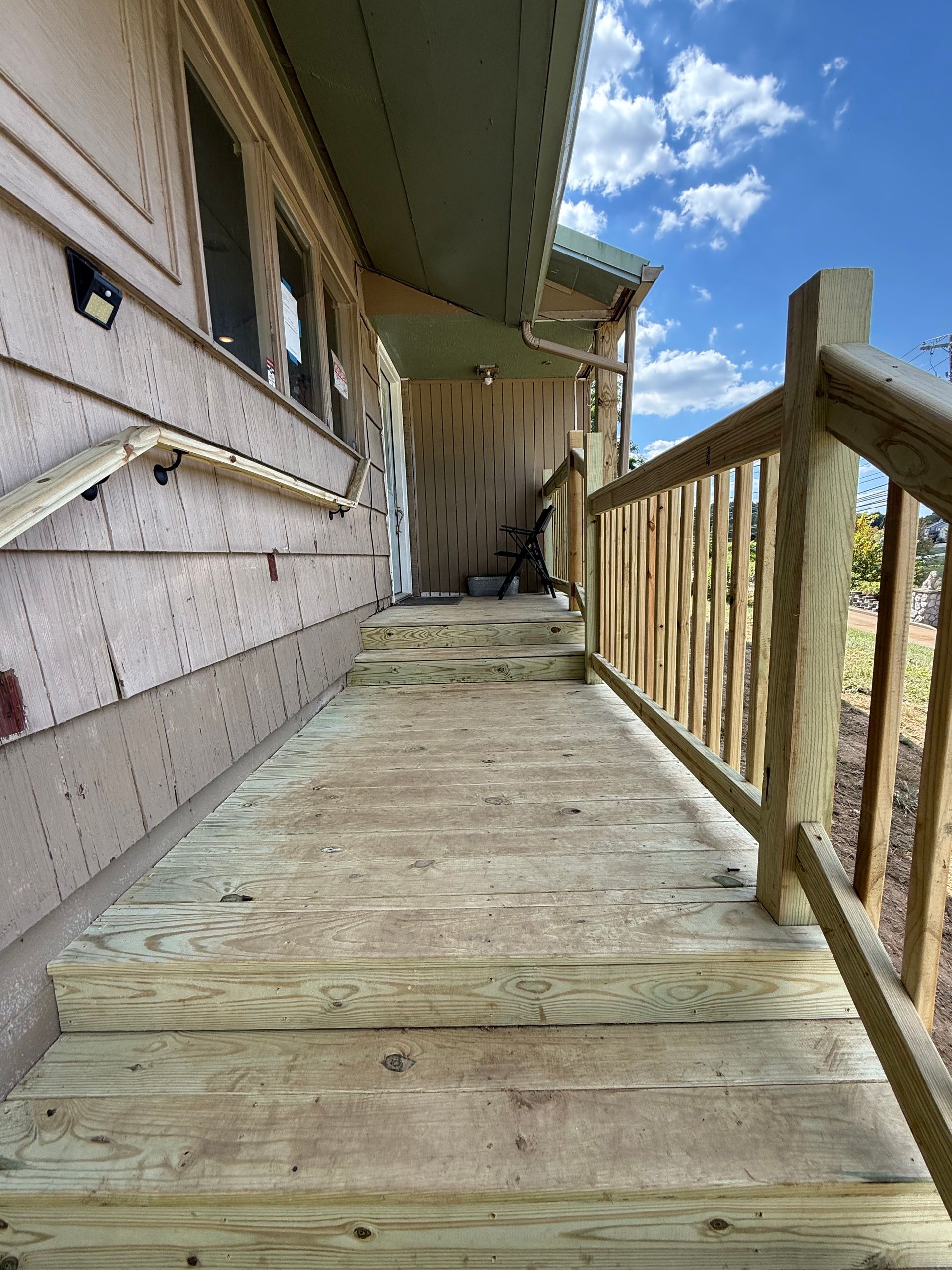 Wooden ramp with railing leading to a house entrance. Green roof, blue sky visible.