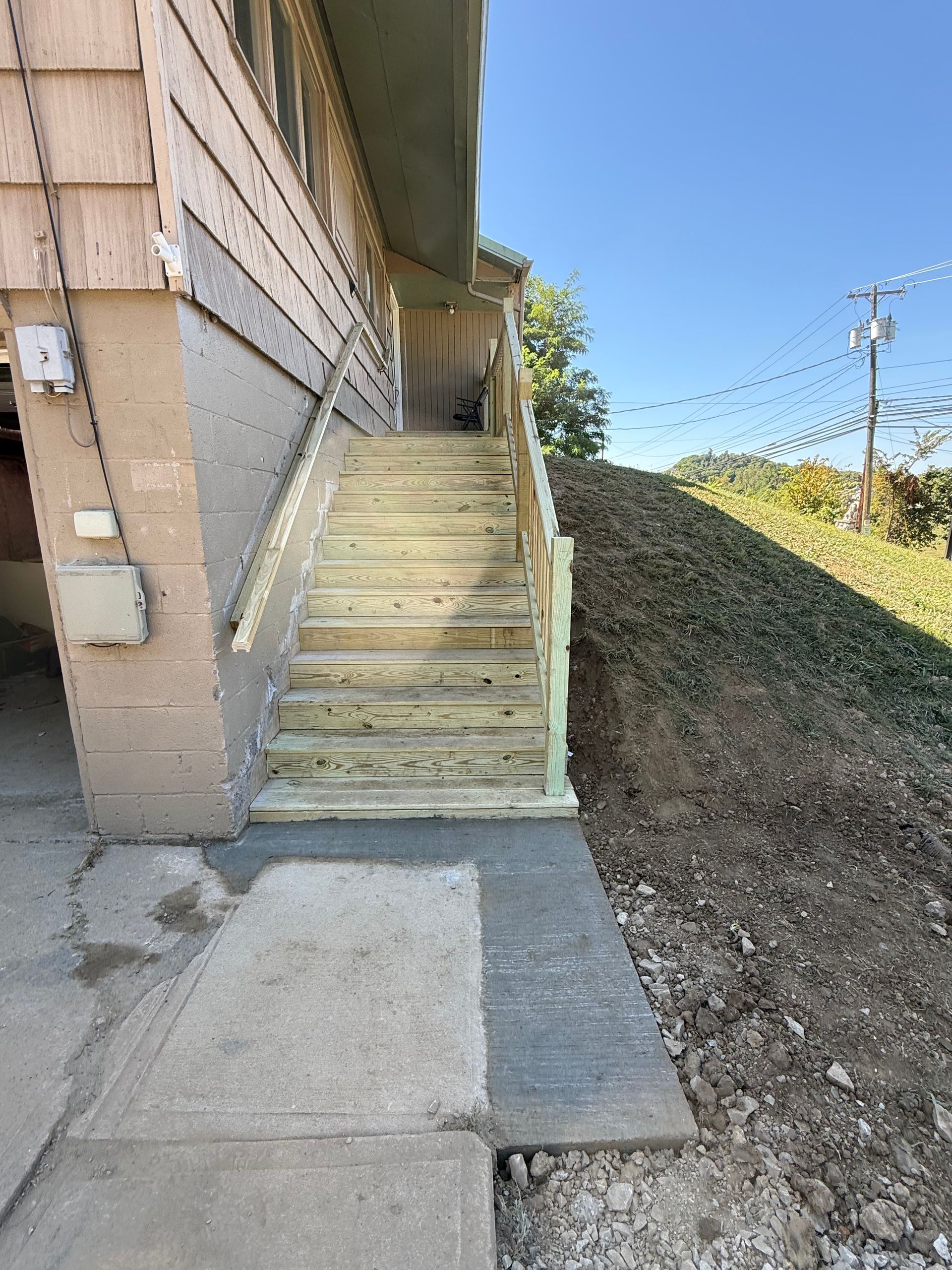 Exterior stairs leading up to a building, constructed of wood and concrete, next to a grassy hill.