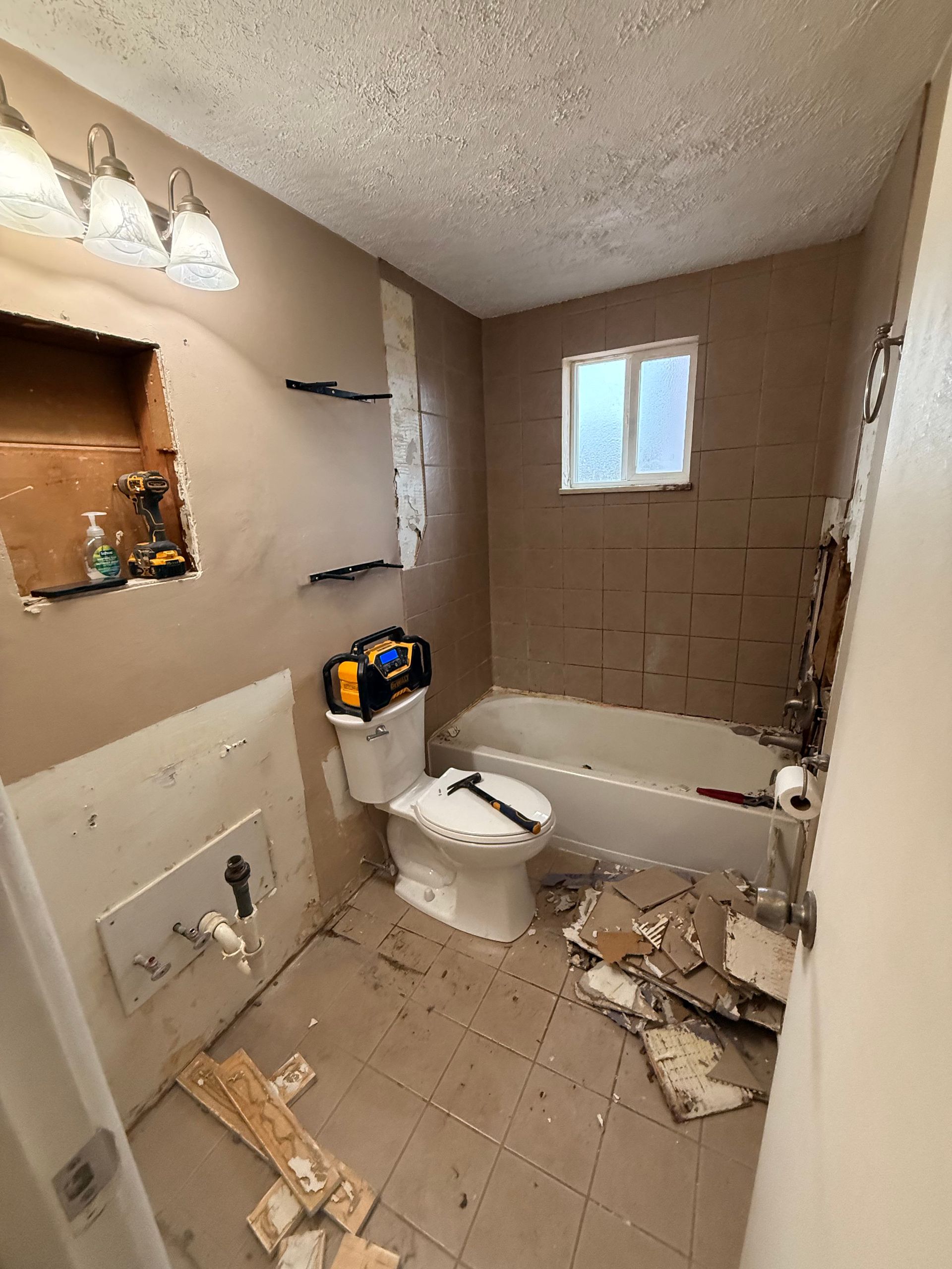 Bathroom under renovation. Walls are torn up. Toilet and bathtub present. Tools and debris on the floor.