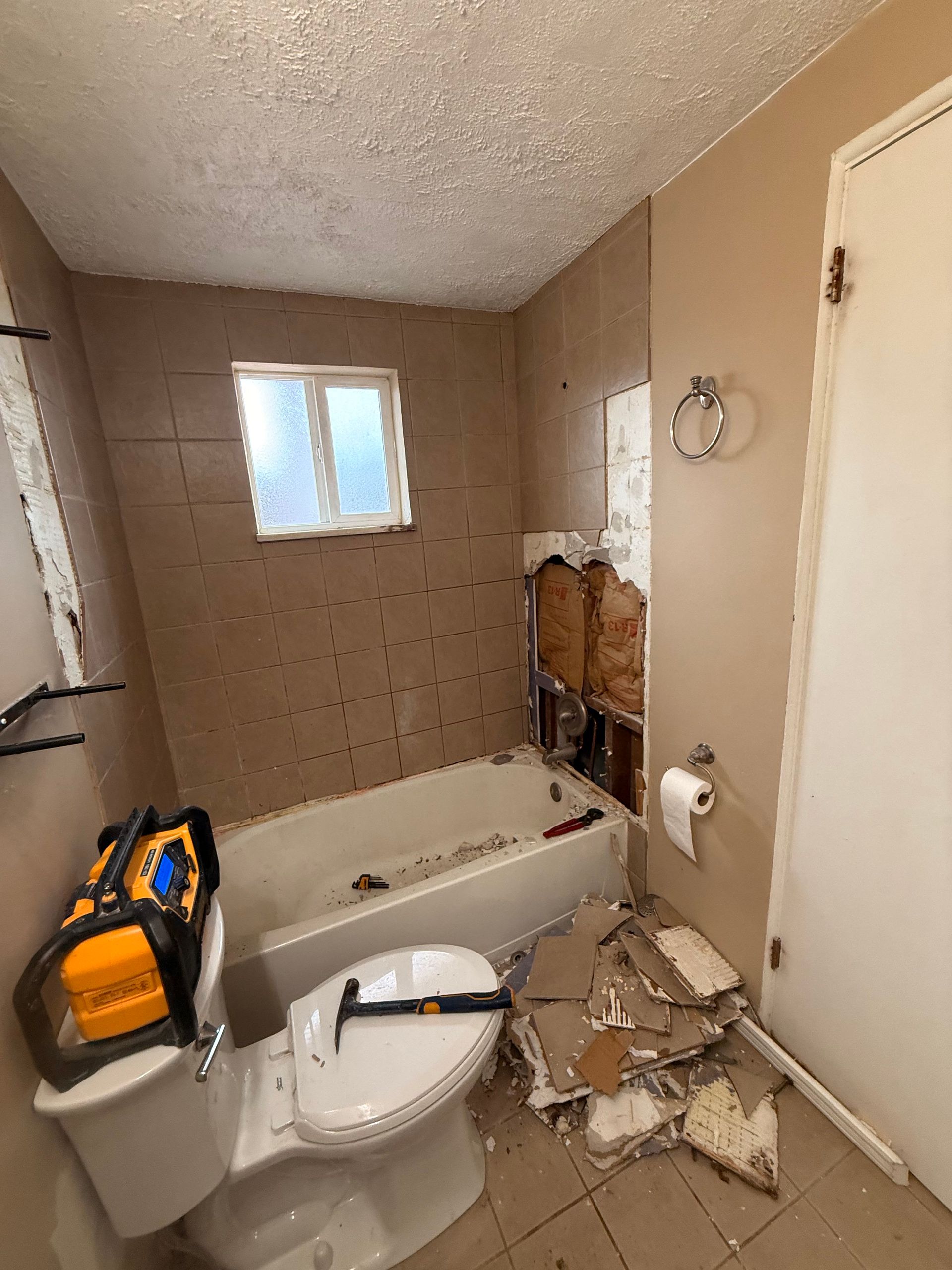Bathroom undergoing renovation, with exposed wall, tub, toilet, tools, and debris.