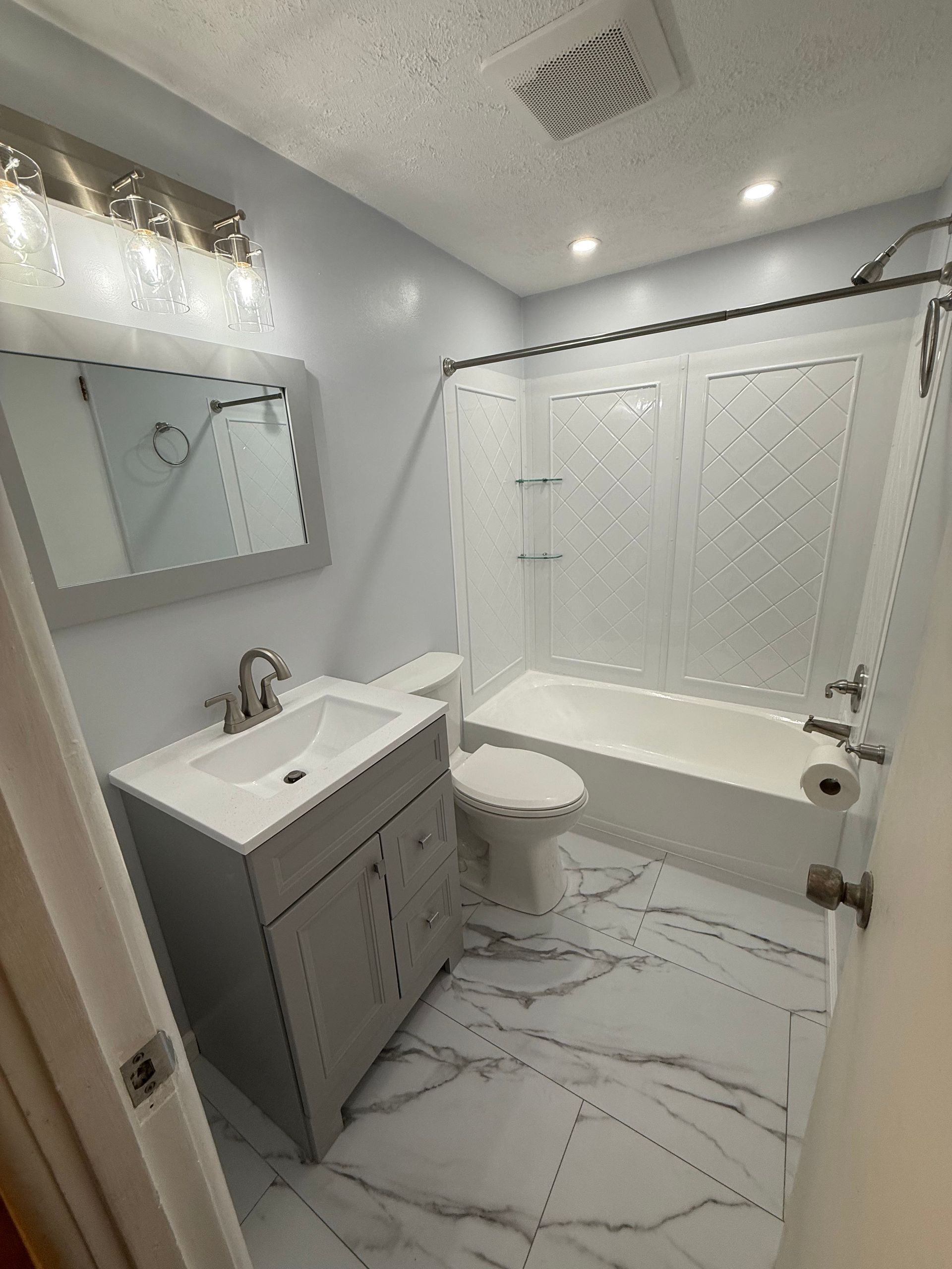 Newly renovated bathroom with white and gray fixtures and marble-look flooring.