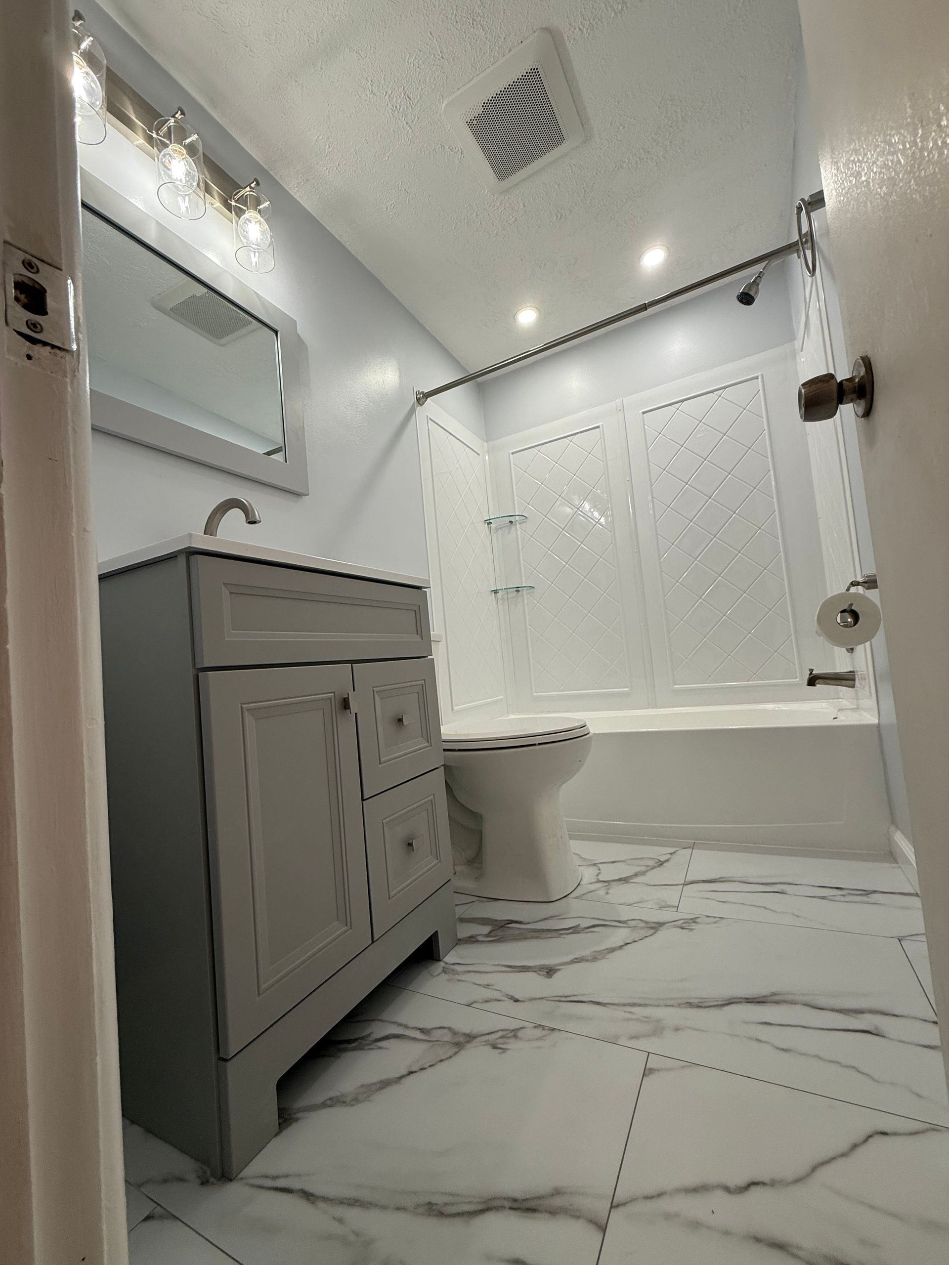 Bathroom with gray vanity, white toilet, bathtub with shower curtain, and marble-look tile floor.