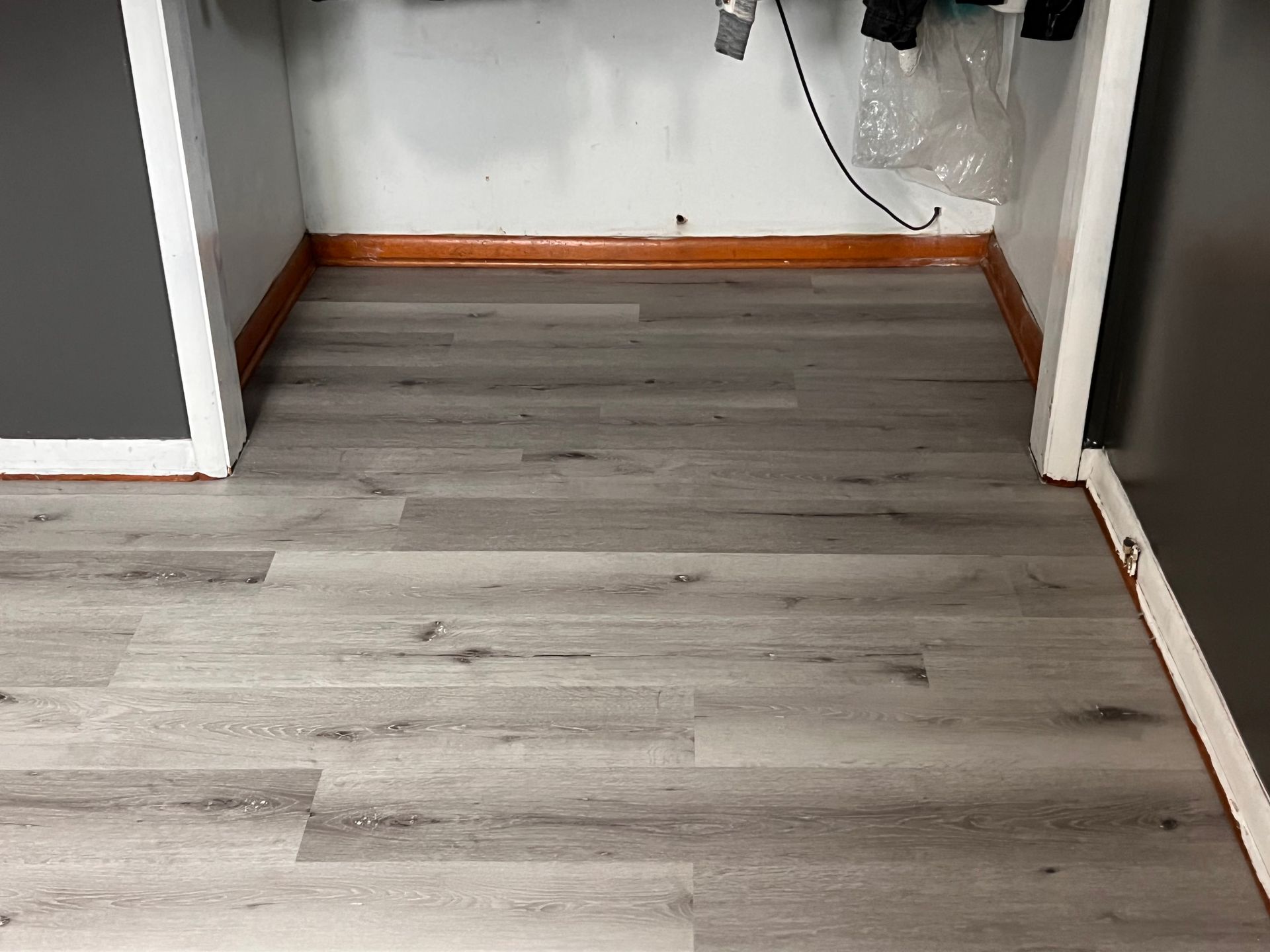 Gray wood-look flooring in a small closet-like space. Orange trim along the base.