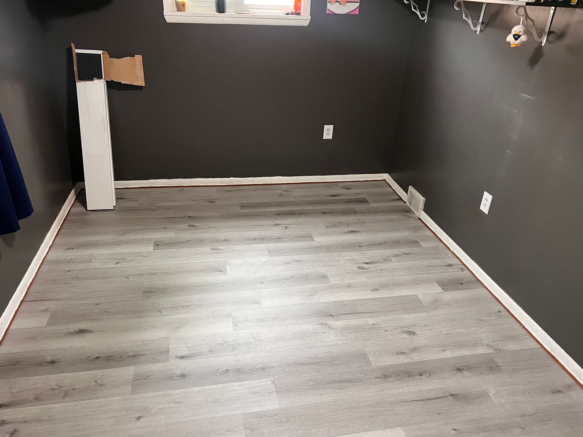 Gray-floored room with dark gray walls, white trim, and a window; mostly empty with a white vertical object.