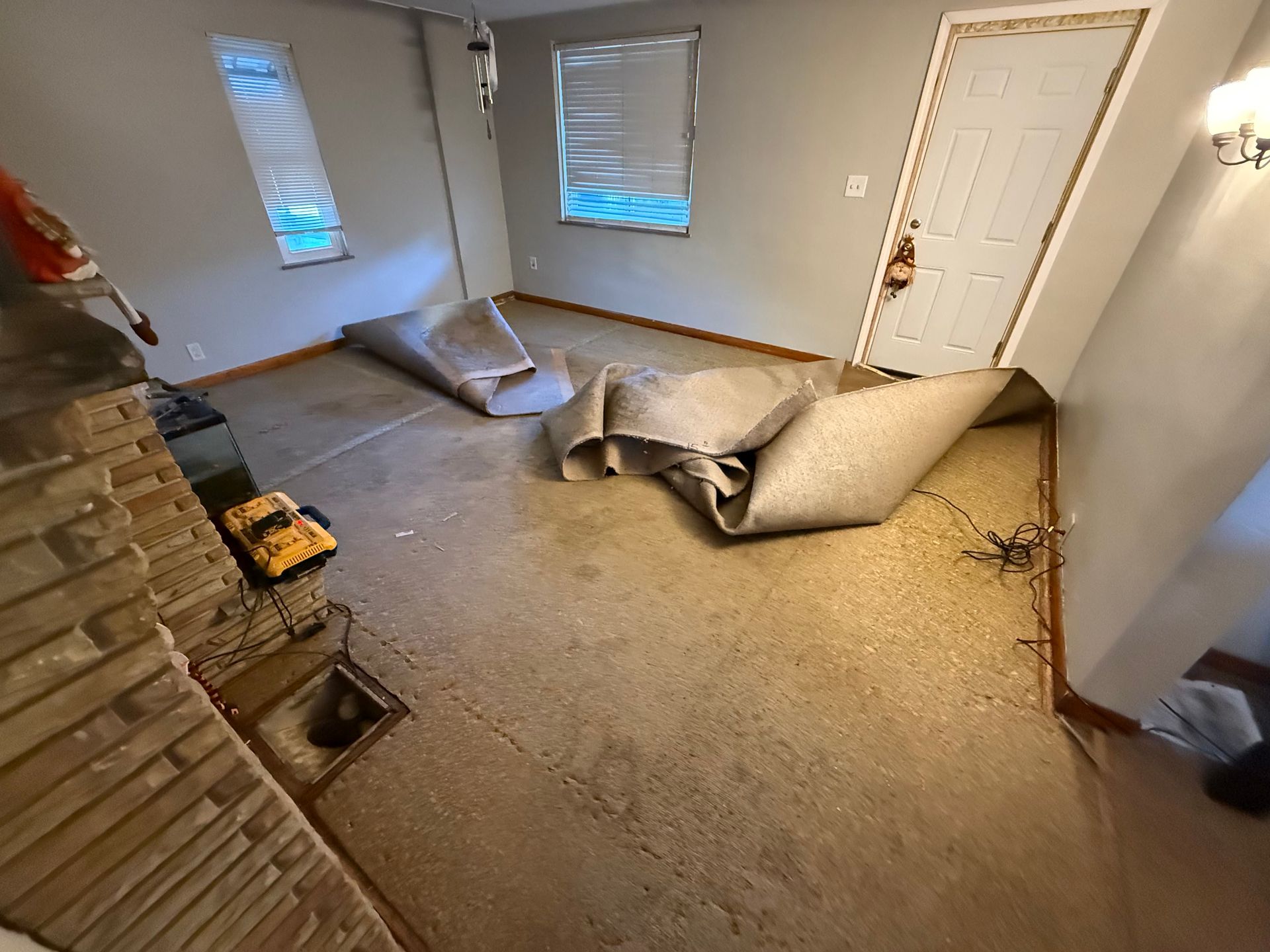 Room with rolled-up carpet, windows, and a doorway. A fireplace is visible on the left.