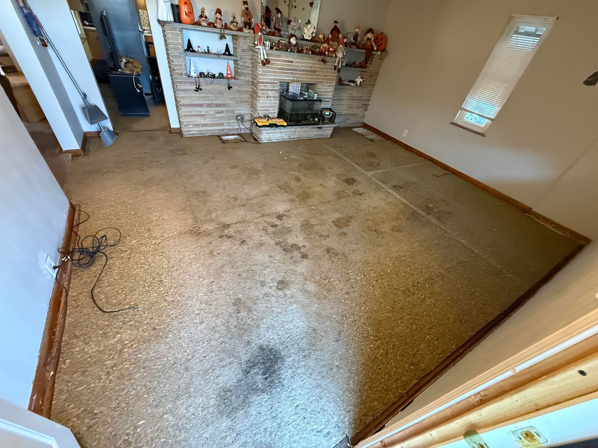 A room with worn, stained carpet, fireplace, and small window.