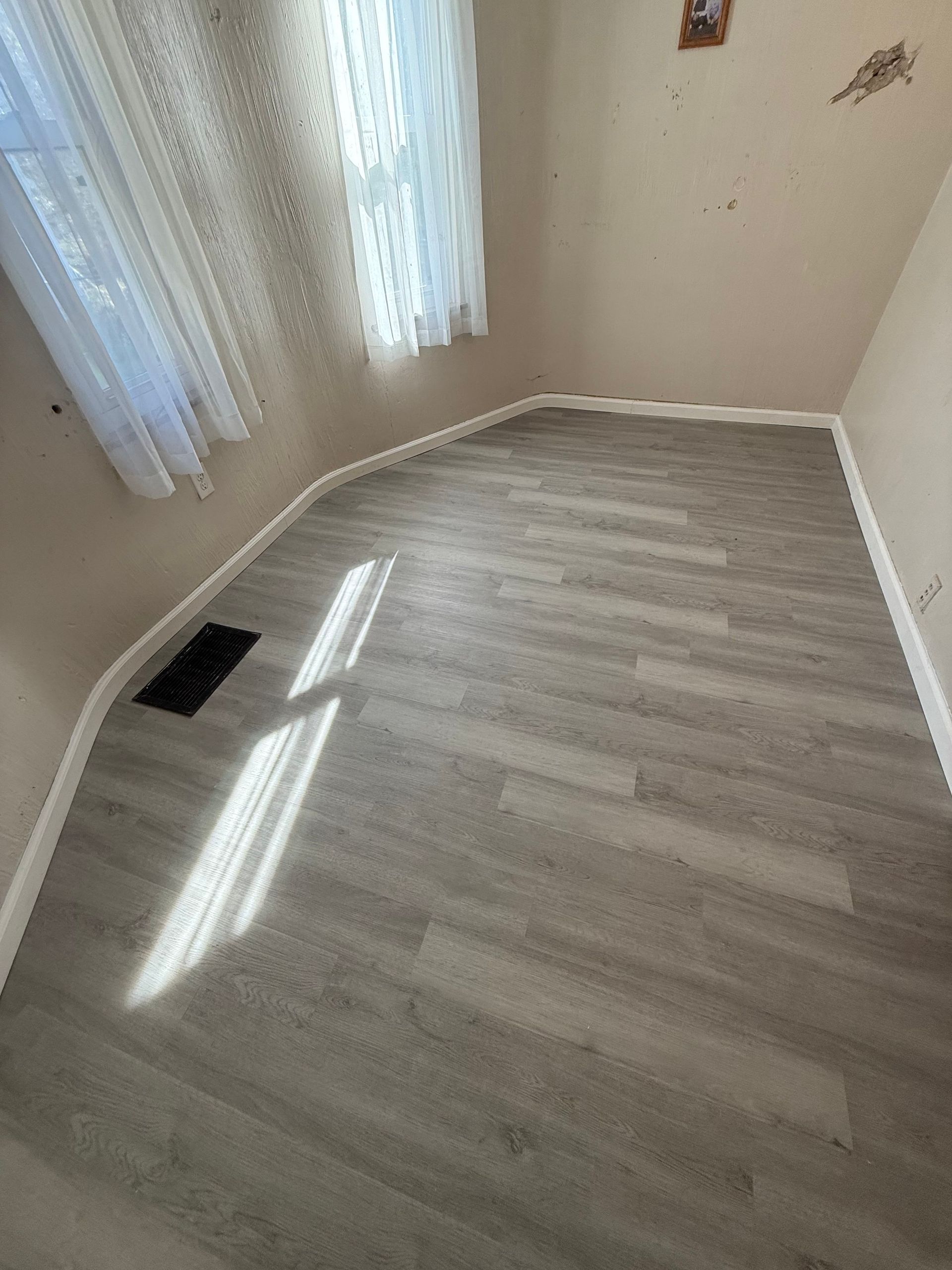 A small room with light gray wood-look flooring and a window with white curtains.