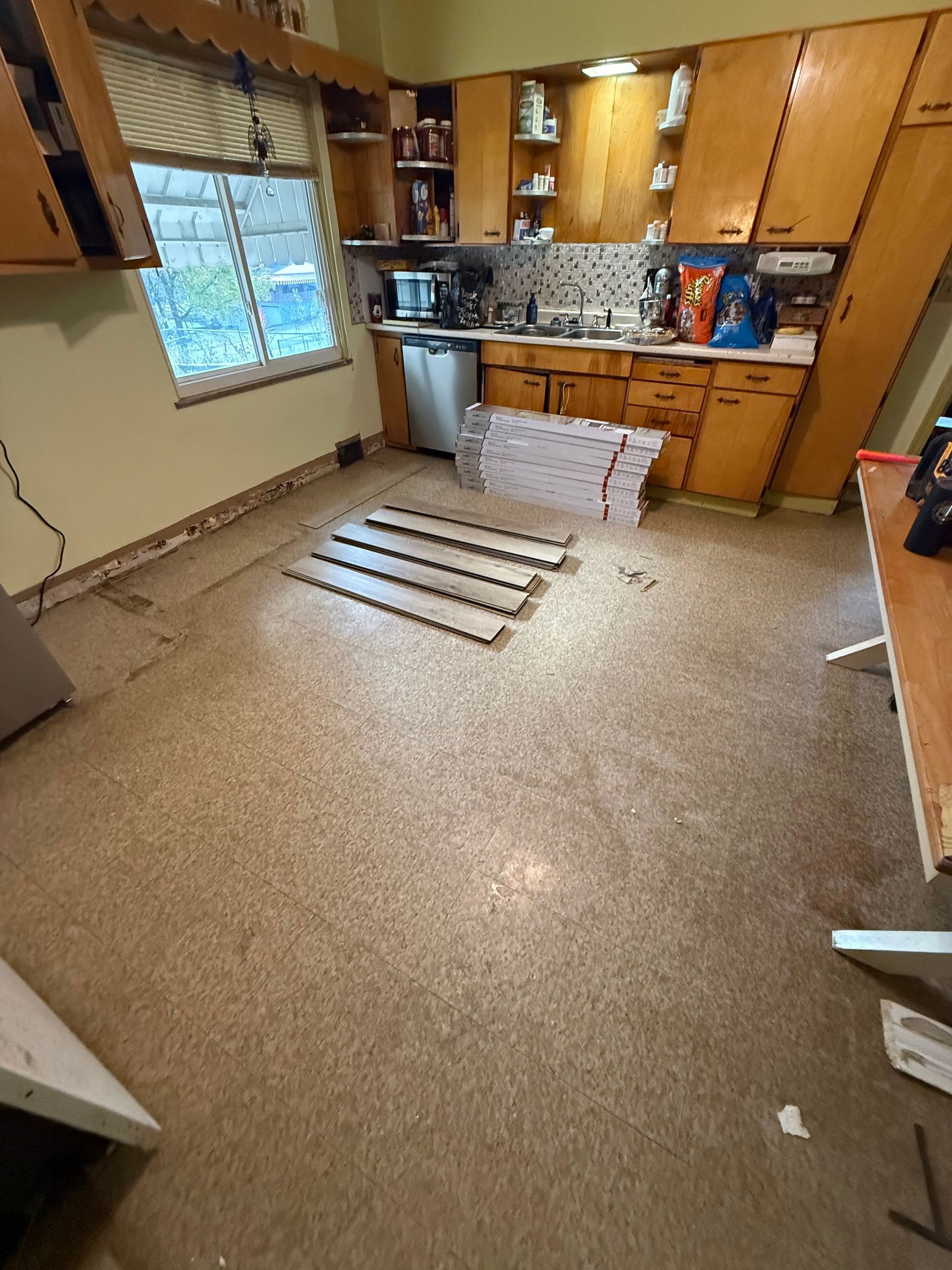 Kitchen with old flooring being replaced; cabinets and a window are visible.