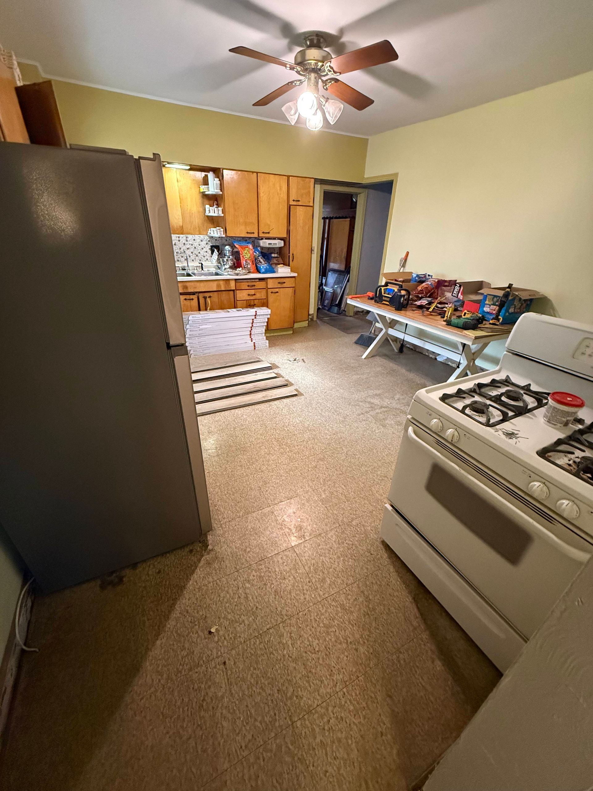 Kitchen with refrigerator, stove, cabinets, and a table covered with objects.
