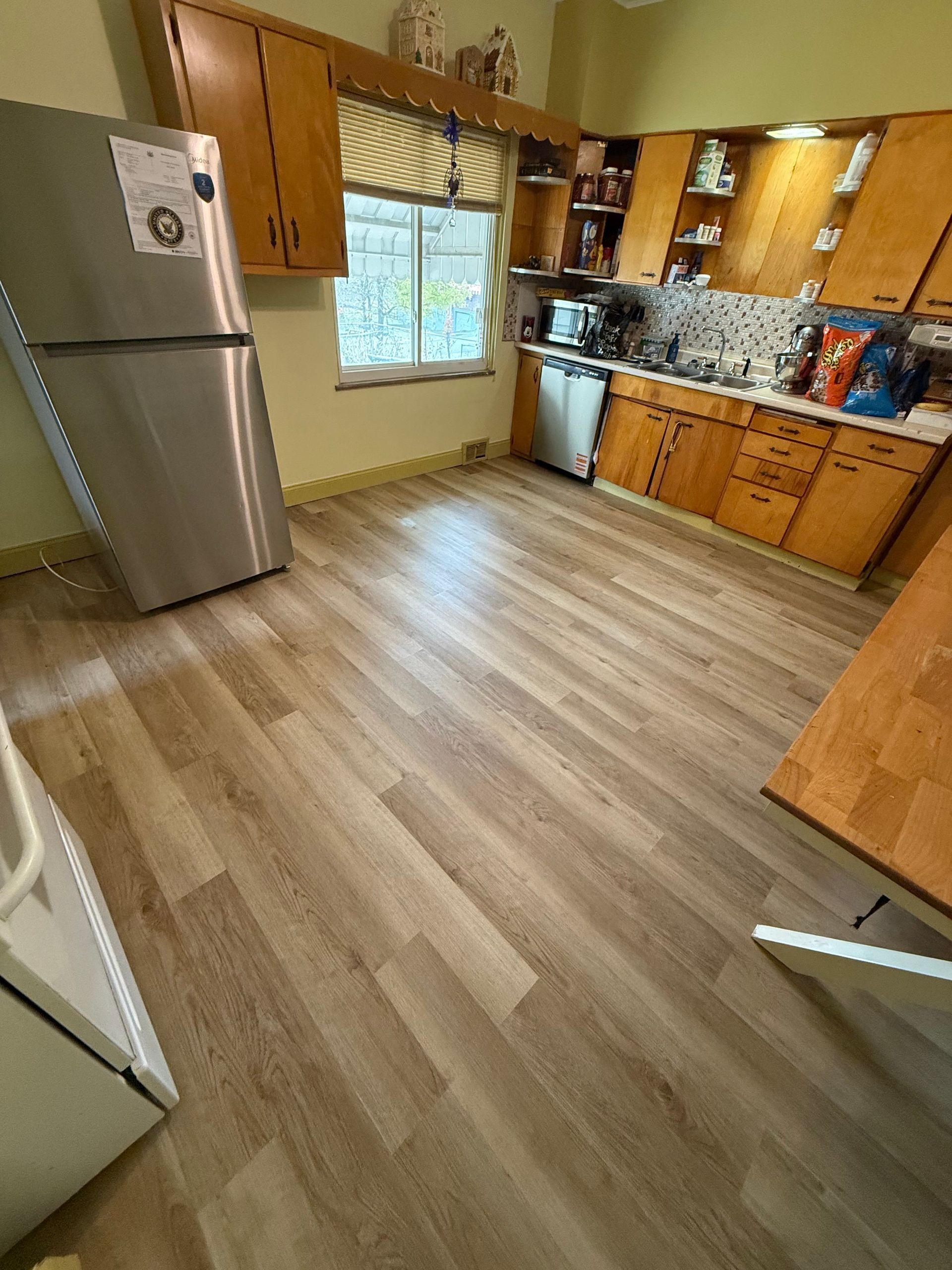 Kitchen with wood cabinets, stainless steel refrigerator, and wood-look flooring.