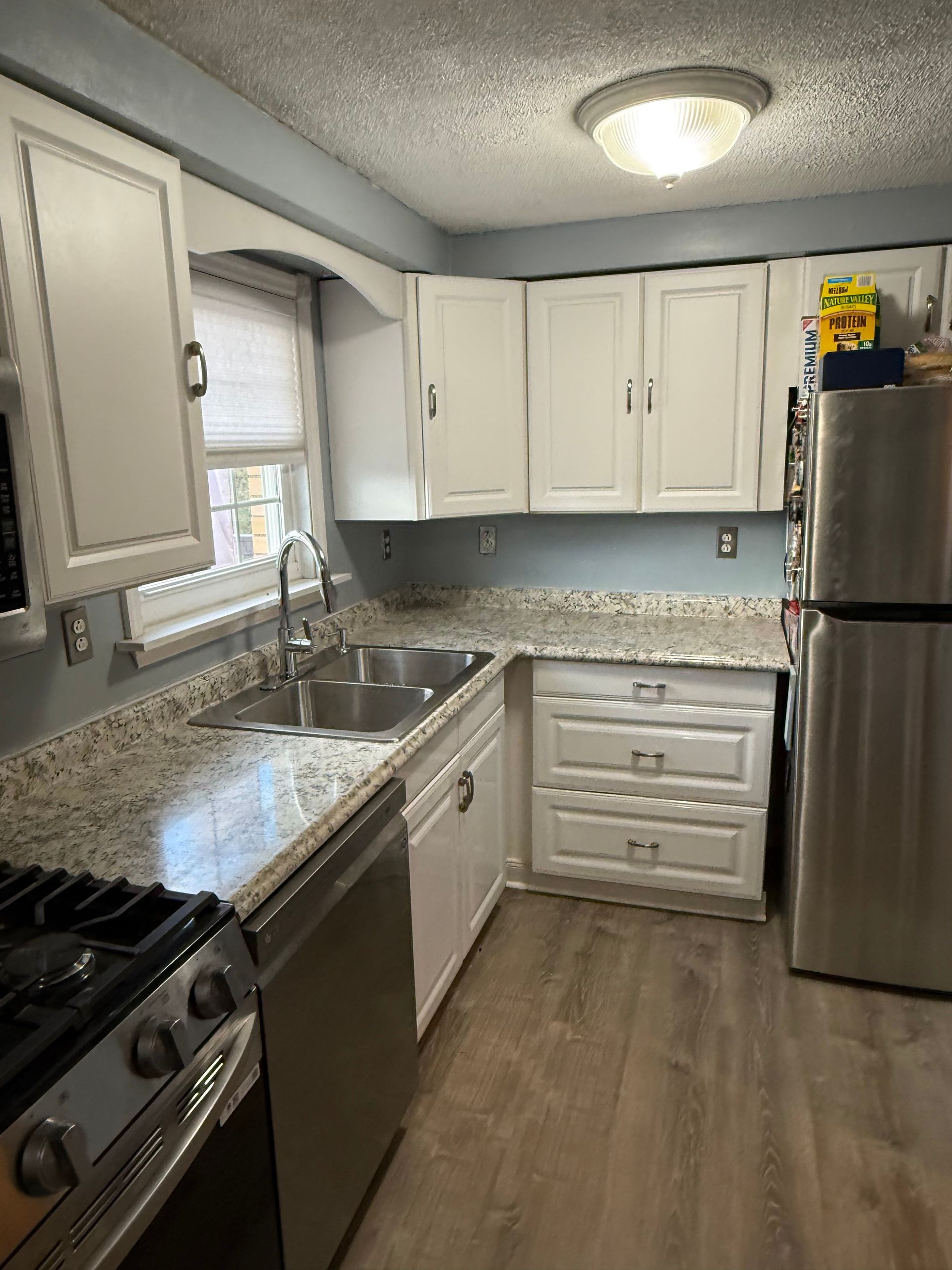 White kitchen with stainless steel appliances, granite countertops, and light blue walls.