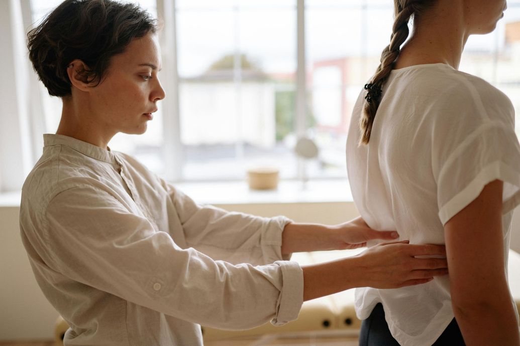 Woman giving back massage in a bright room with a window; both wearing light-colored tops.