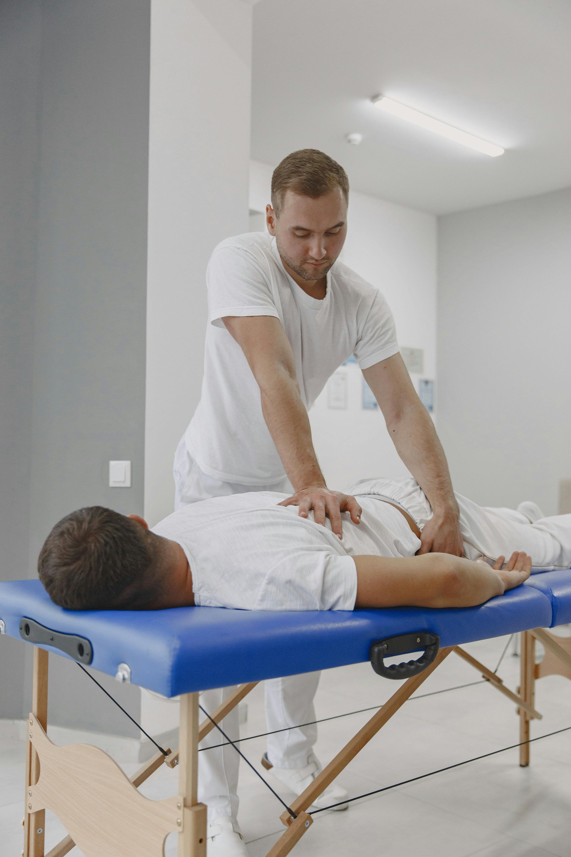 Therapist in white clothing giving abdominal massage to a man lying on a blue massage table.