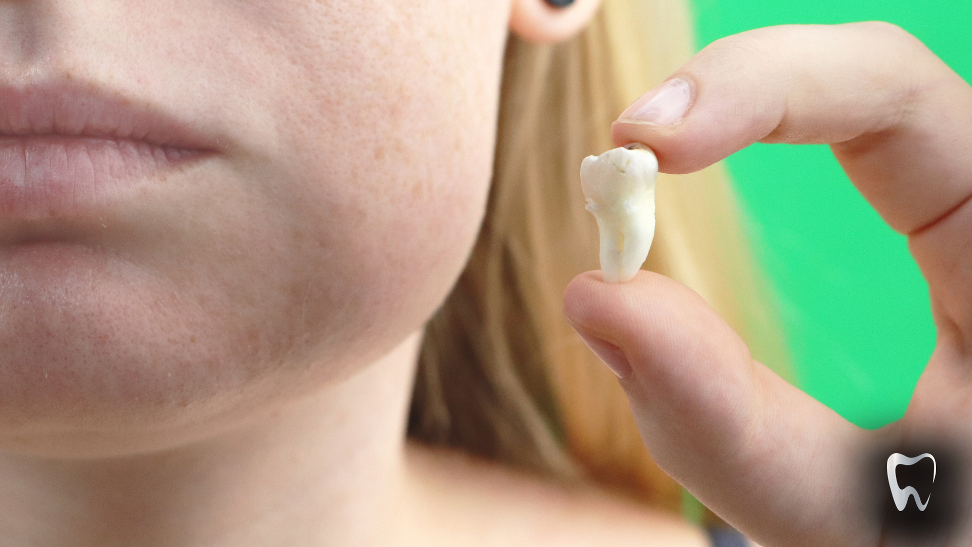 A woman is holding a tooth in her hand in front of her face.