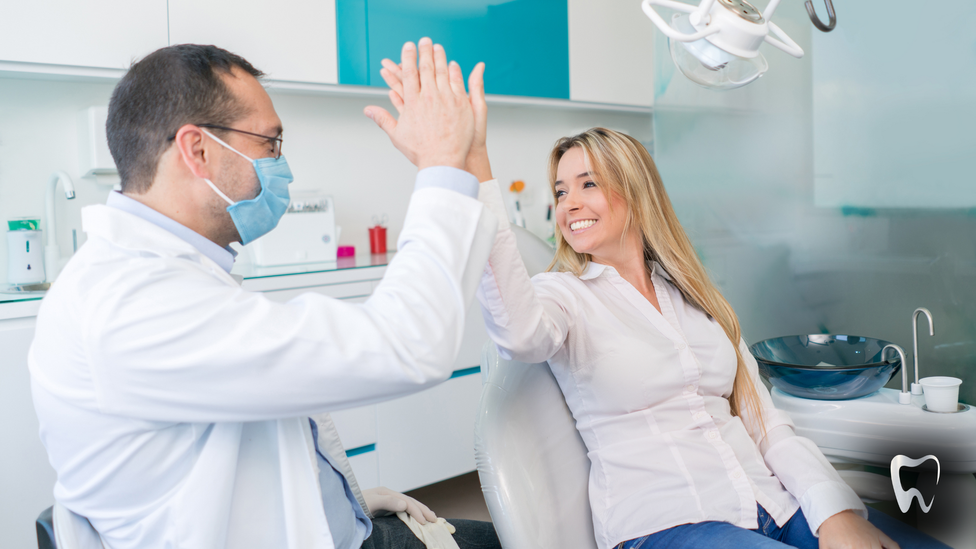 A dentist and a patient are giving each other a high five in a dental office.