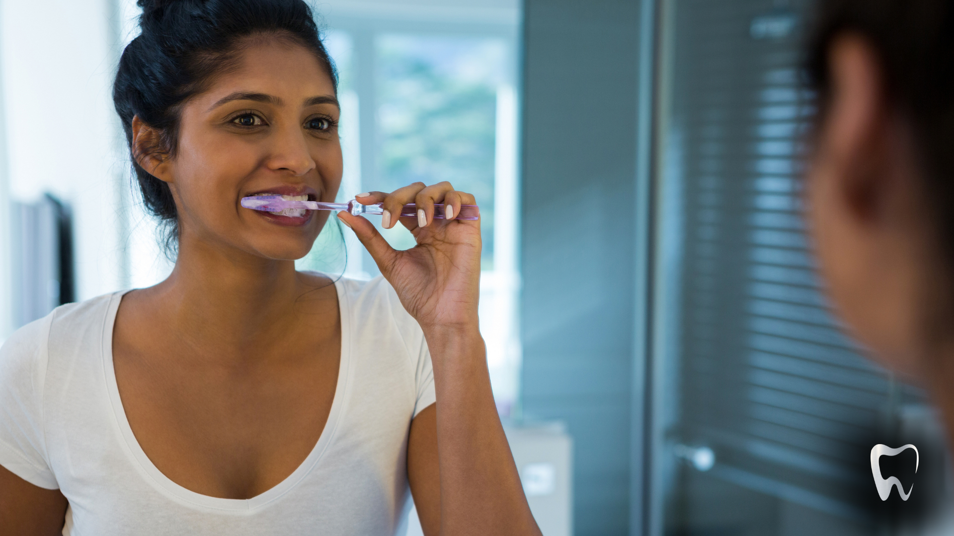 A woman is brushing her teeth in front of a mirror.