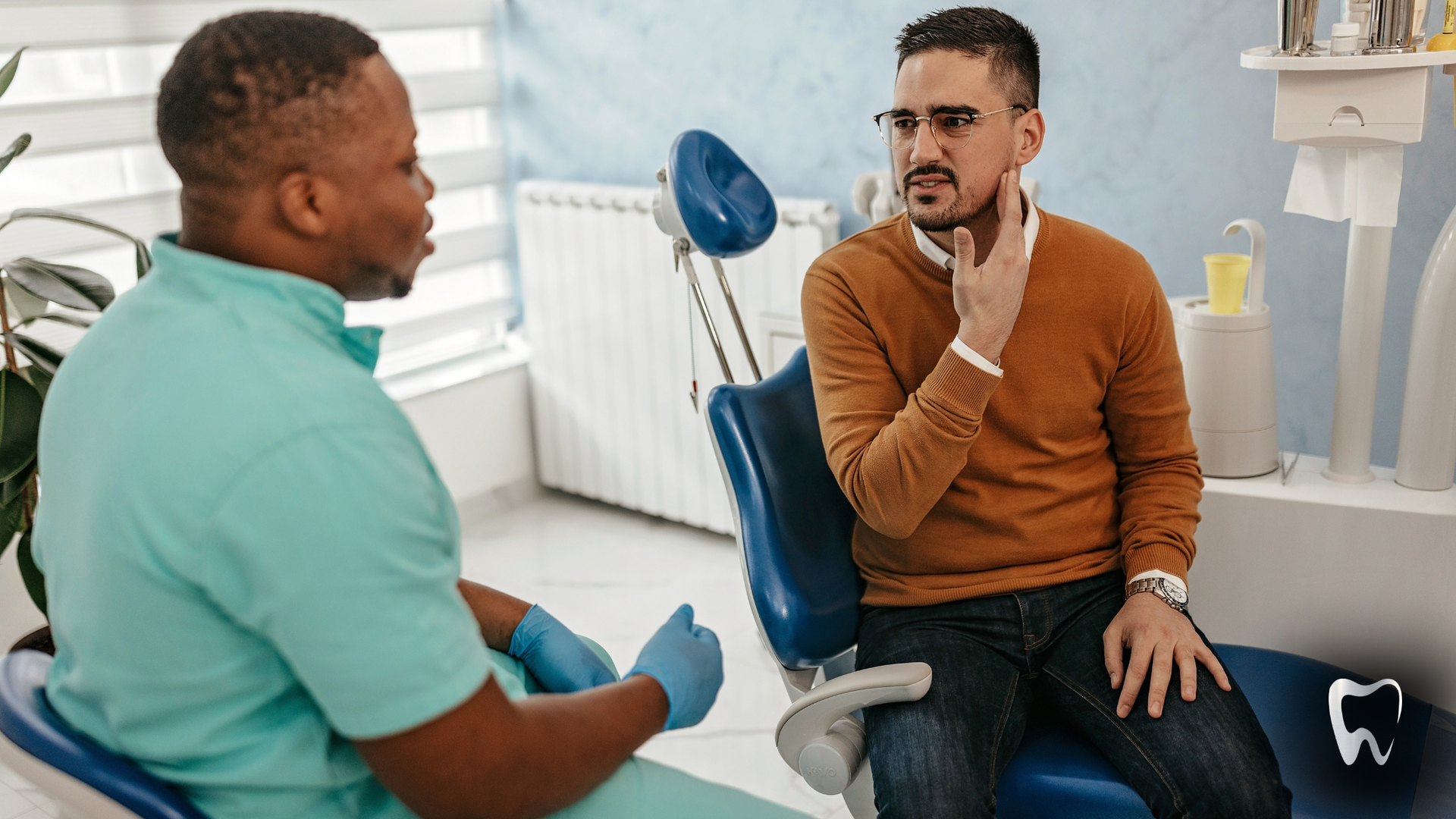 A man is sitting in a dental chair talking to a dentist.