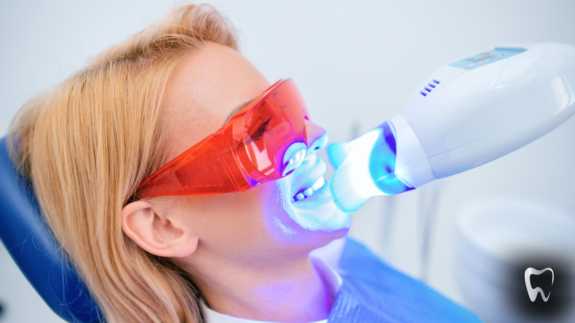 Woman in dental chair undergoing teeth whitening with UV light and protective glasses.