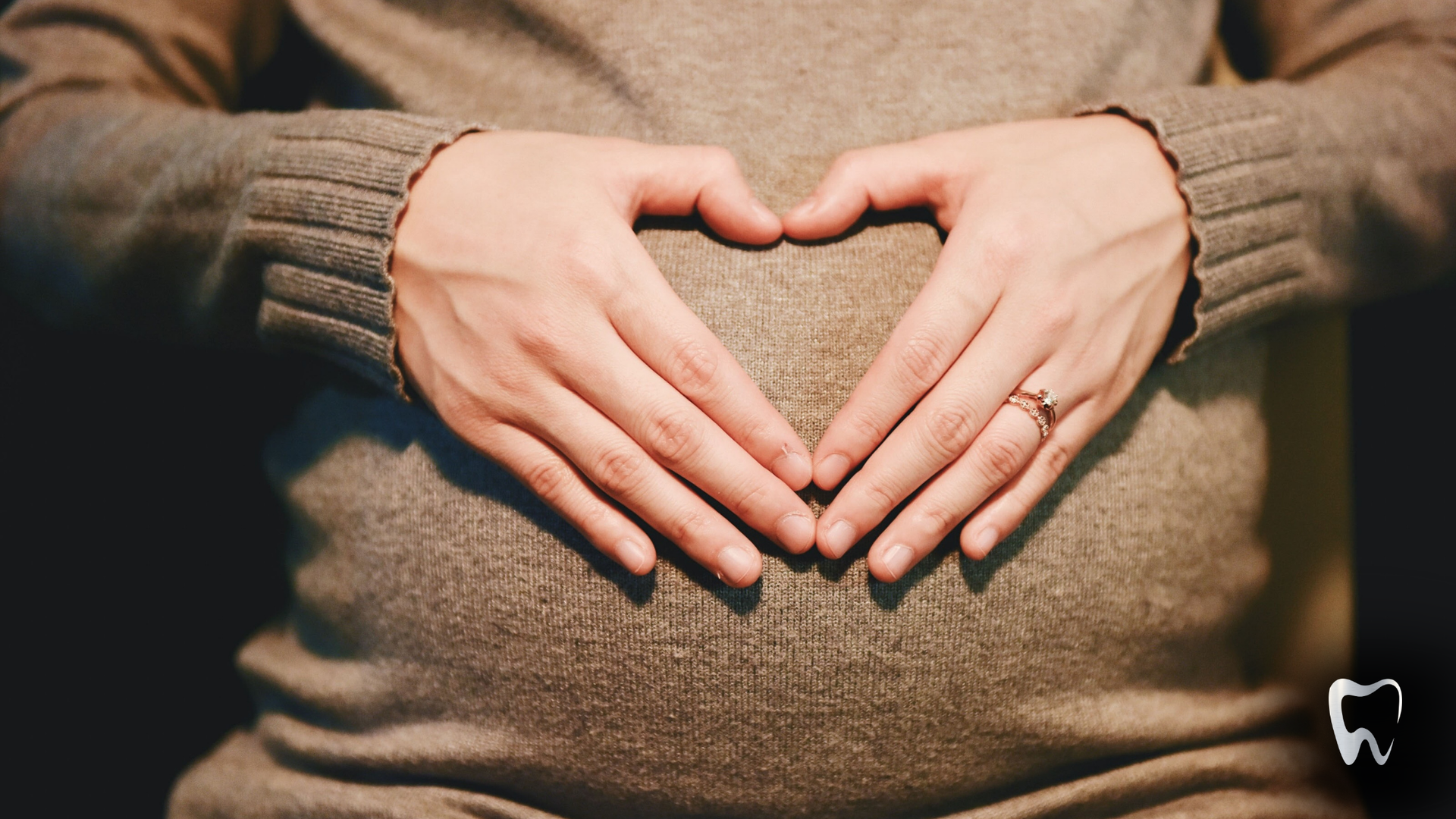 A pregnant woman is making a heart shape with her hands on her belly.