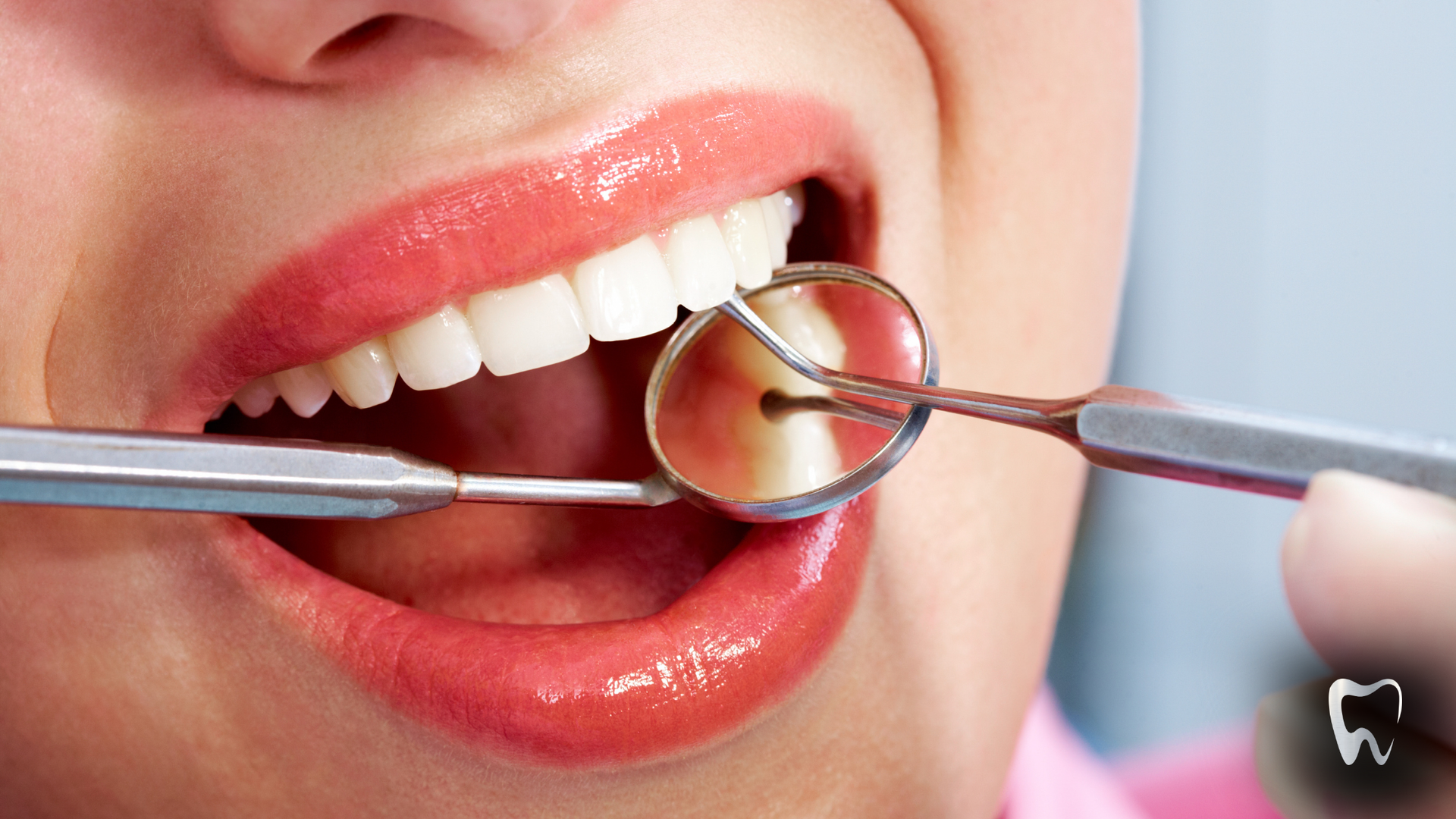 Person's mouth open with dental tools; teeth examined with mirror, glossy lips.