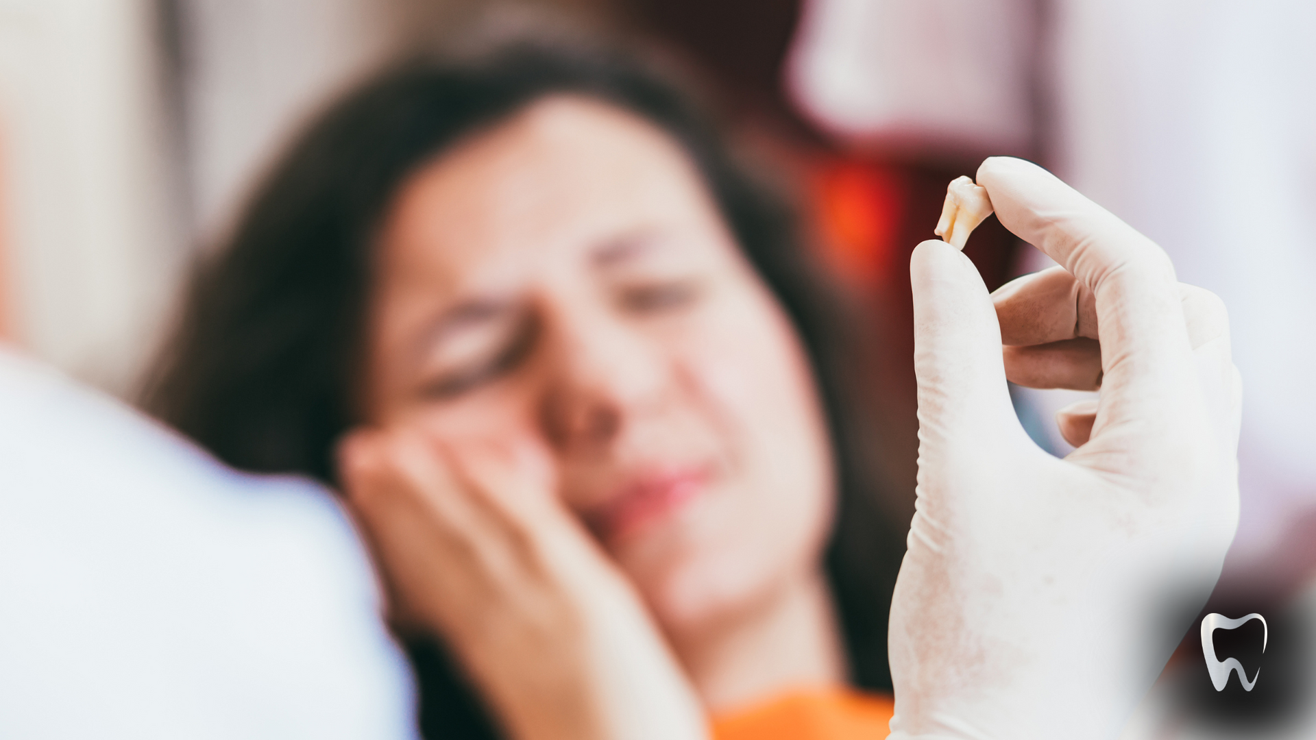 A dentist is holding a tooth in front of a woman with a toothache.