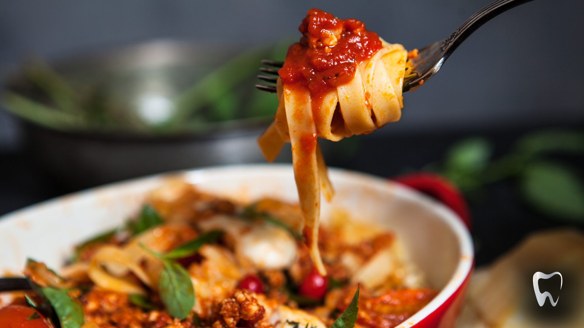 A close up of a fork holding a piece of pasta over a bowl of pasta.