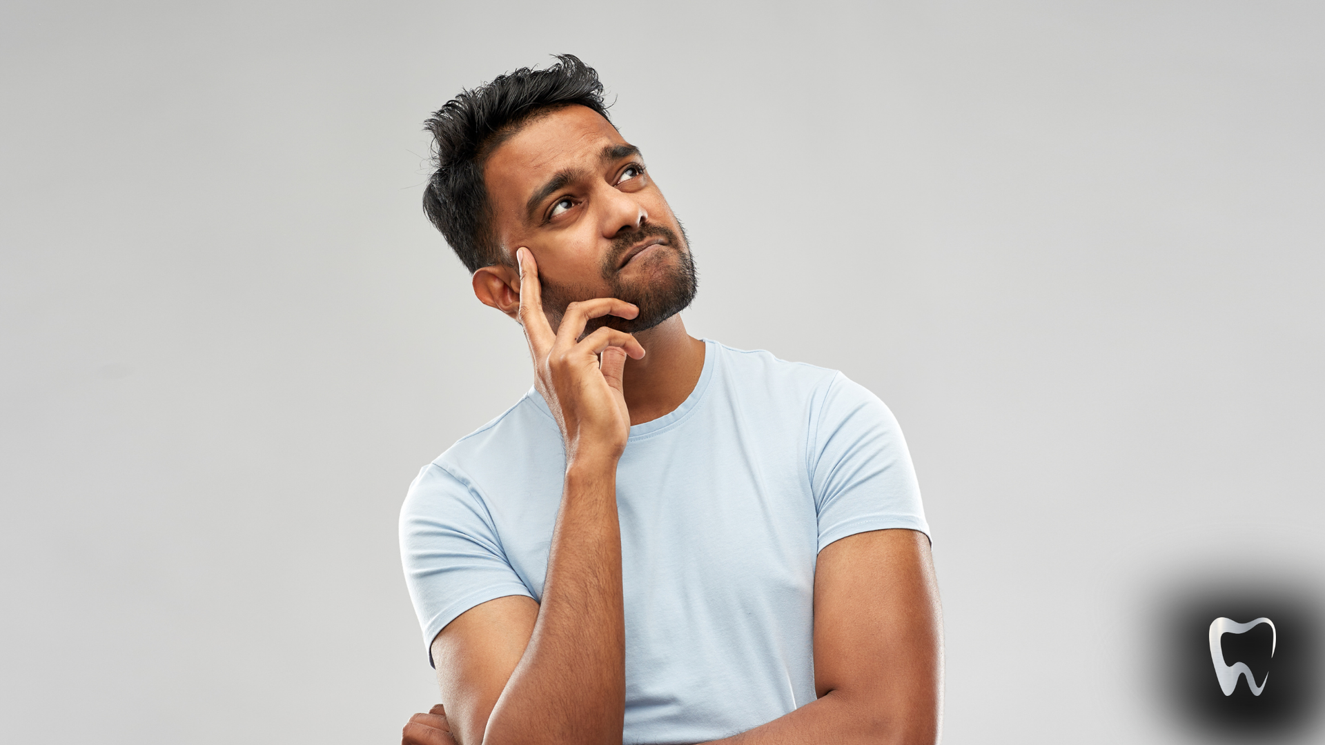 Man in a light blue shirt, hand on chin, looking upwards thoughtfully. Gray background.